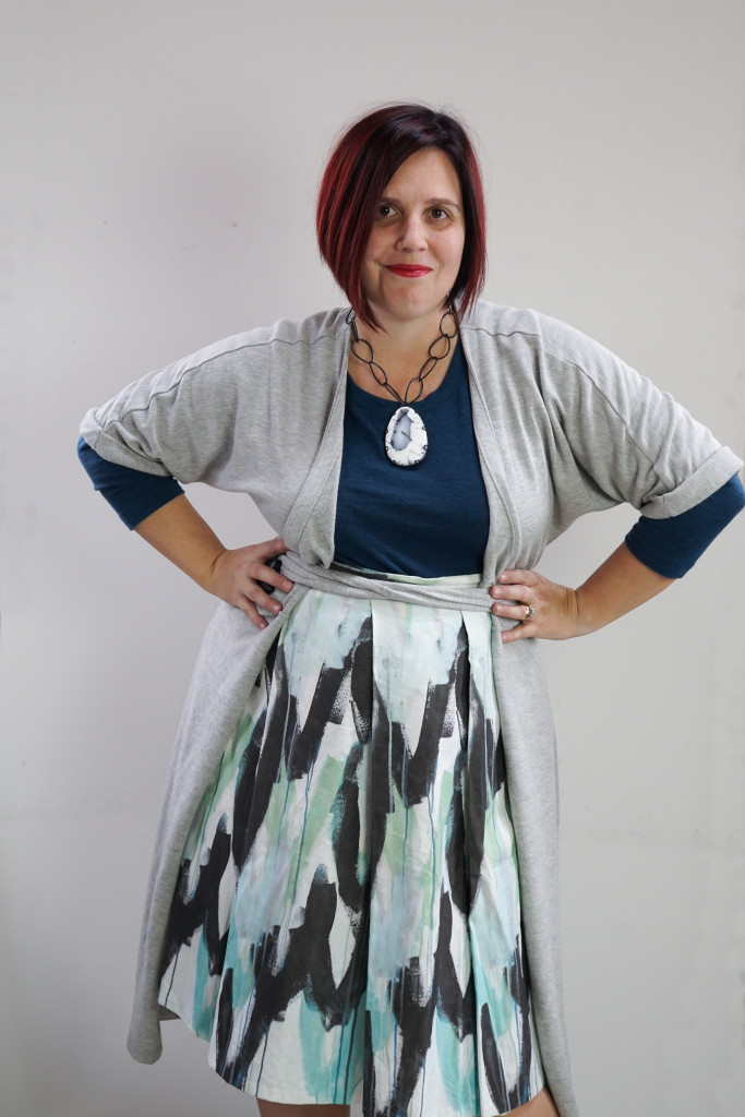 one dress challenge, creative capsule outfit inspiration: wrap dress as a duster over a patterned skirt and teal sweater with a bold gemstone necklace