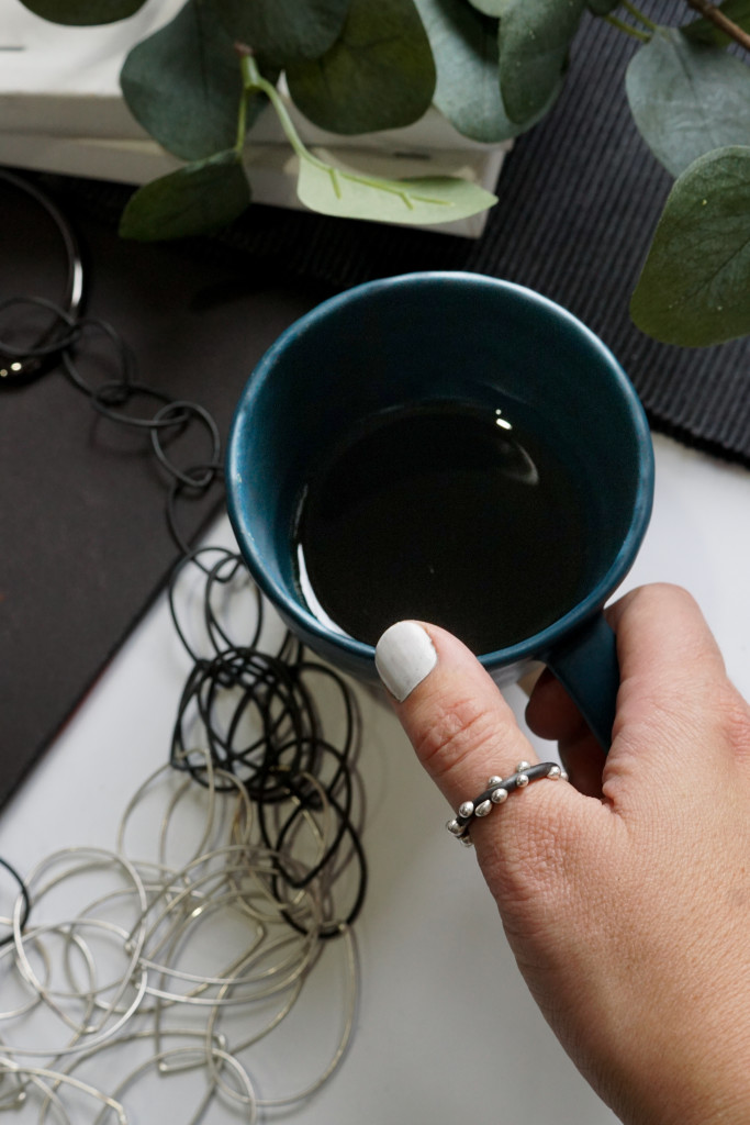 artist maker morning flatlay: handmade ceramic tea cup, mixed metal chain link statement necklace, handmade silver on steel thumb ring