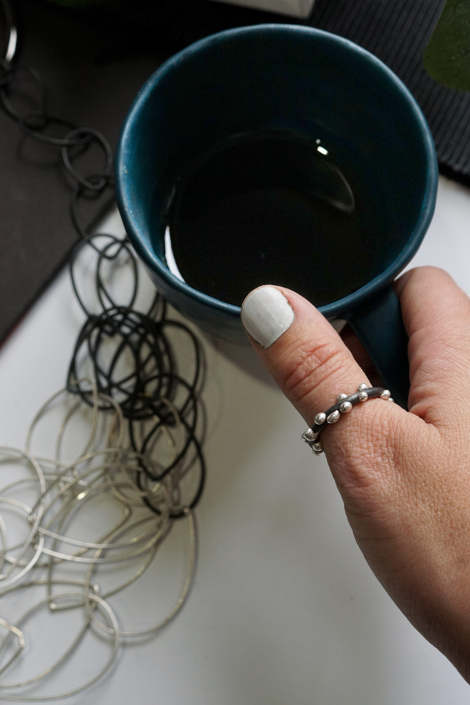 artist maker morning flatlay: handmade ceramic tea cup, mixed metal chain link statement necklace, handmade silver on steel thumb ring