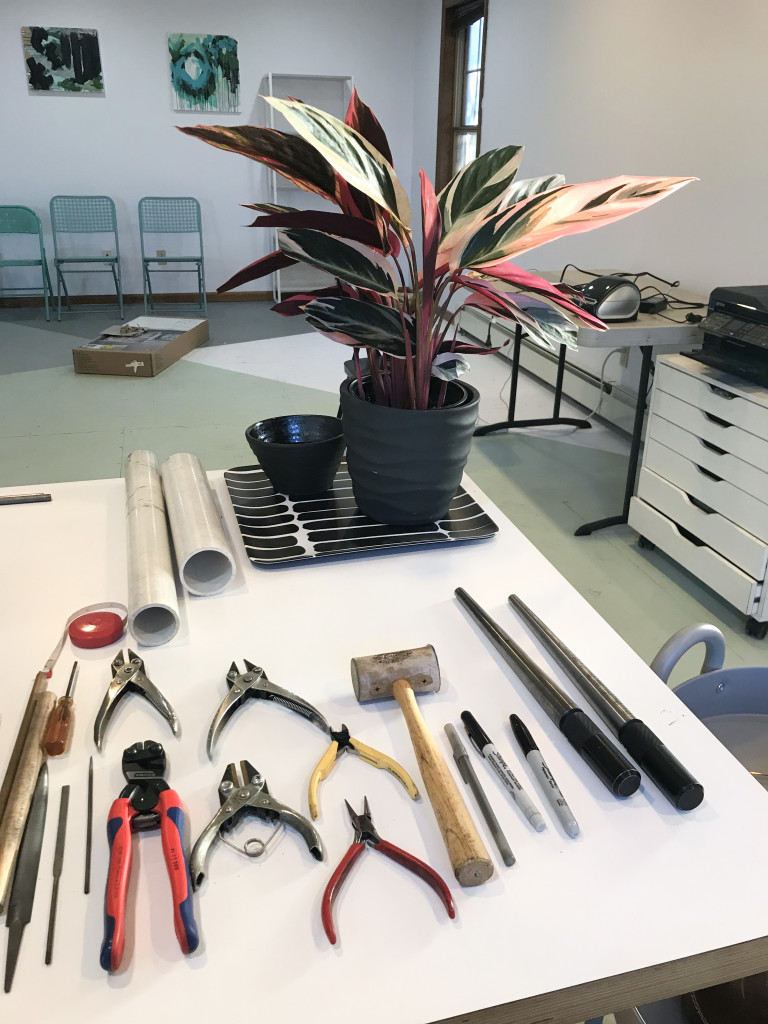 jewelry studio with metalsmithing tools, plant, paintings, and painted plywood floor