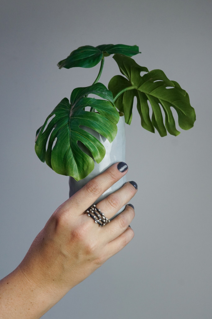 faux monsterra plant,  handmade ceramic vase, and mixed metal stacking rings