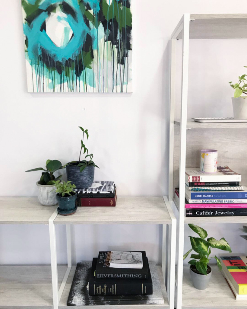 peperomia plants and paintings on bookshelf in metalsmithing studio