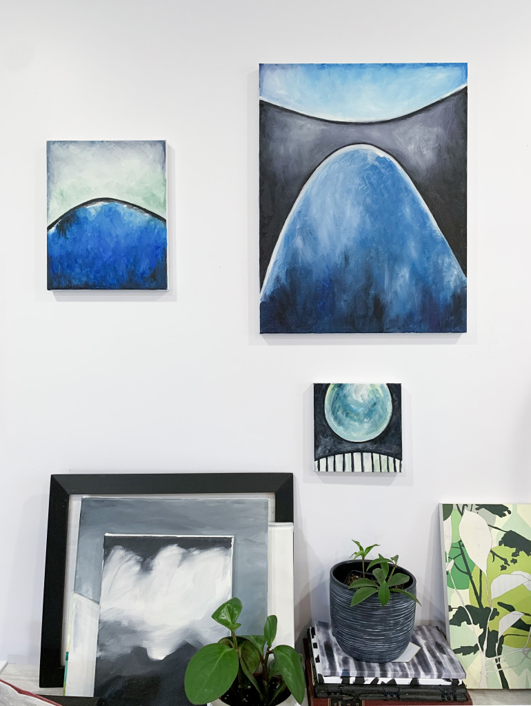 modern art original paintings by megan auman hanging above a shelf with plants and more paintings