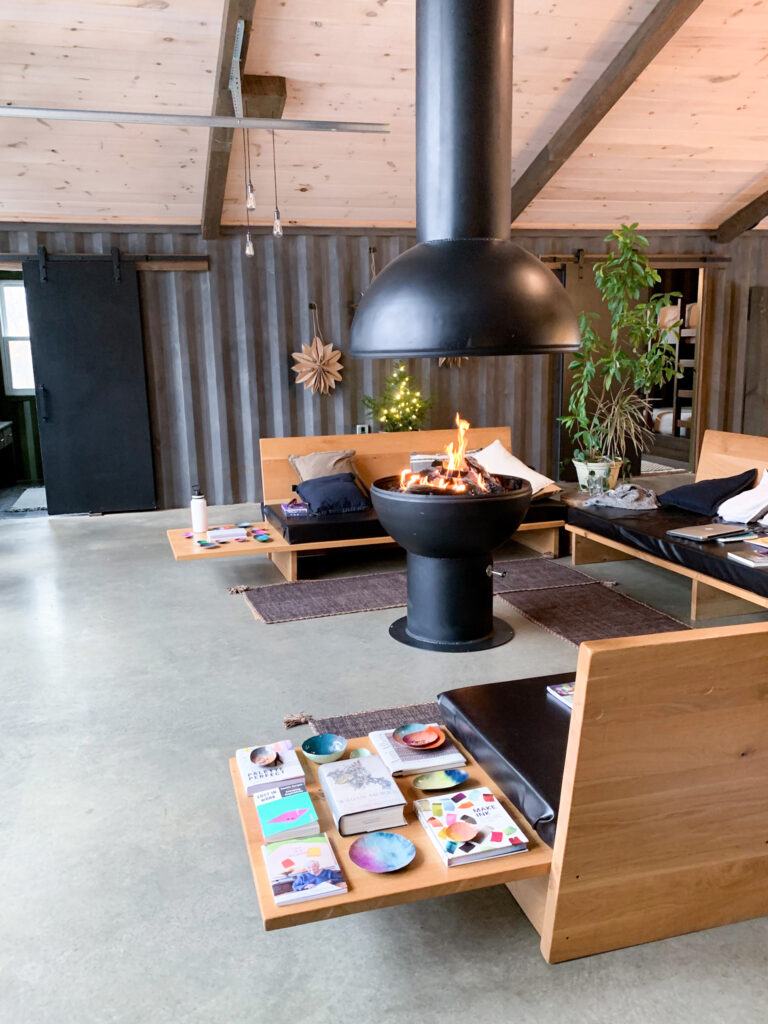 books on art and decorative copper dishes displayed on a side table in a cabin in the woods with a large open gas fire pit and modern couches