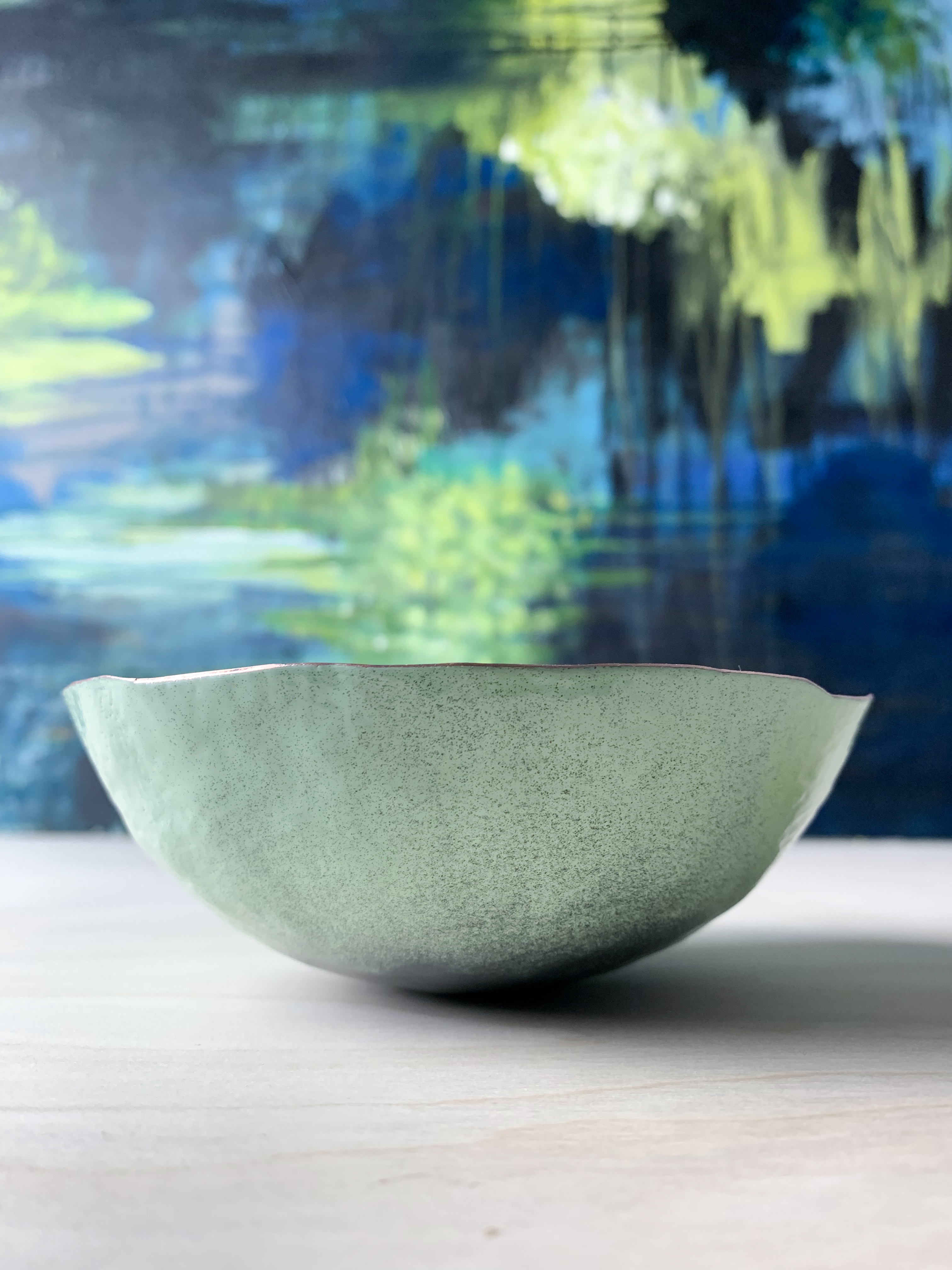 colorful decorative metal raised copper bowl in front of abstract expressionist painting