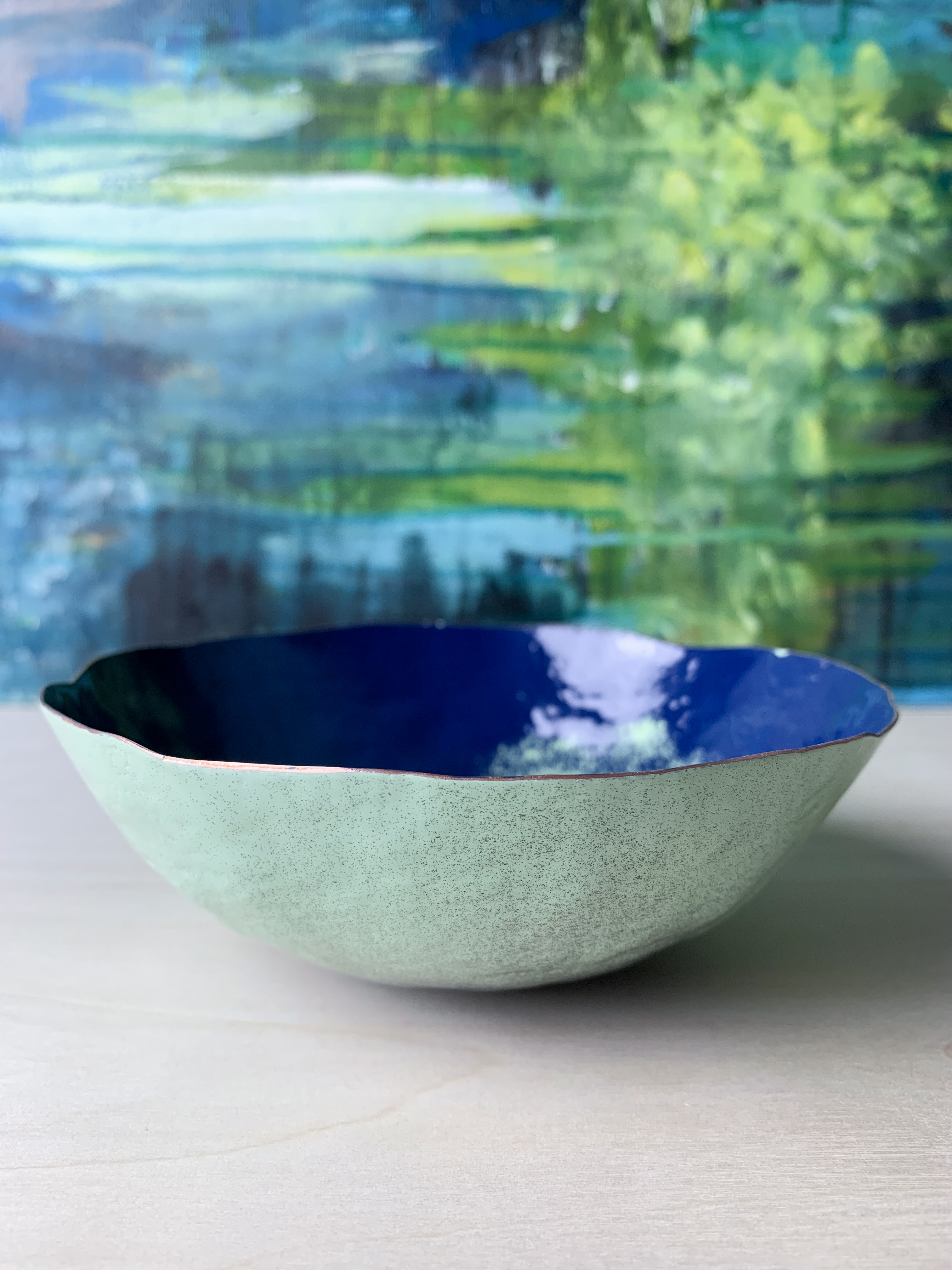 colorful decorative metal raised copper bowl in front of abstract expressionist painting
