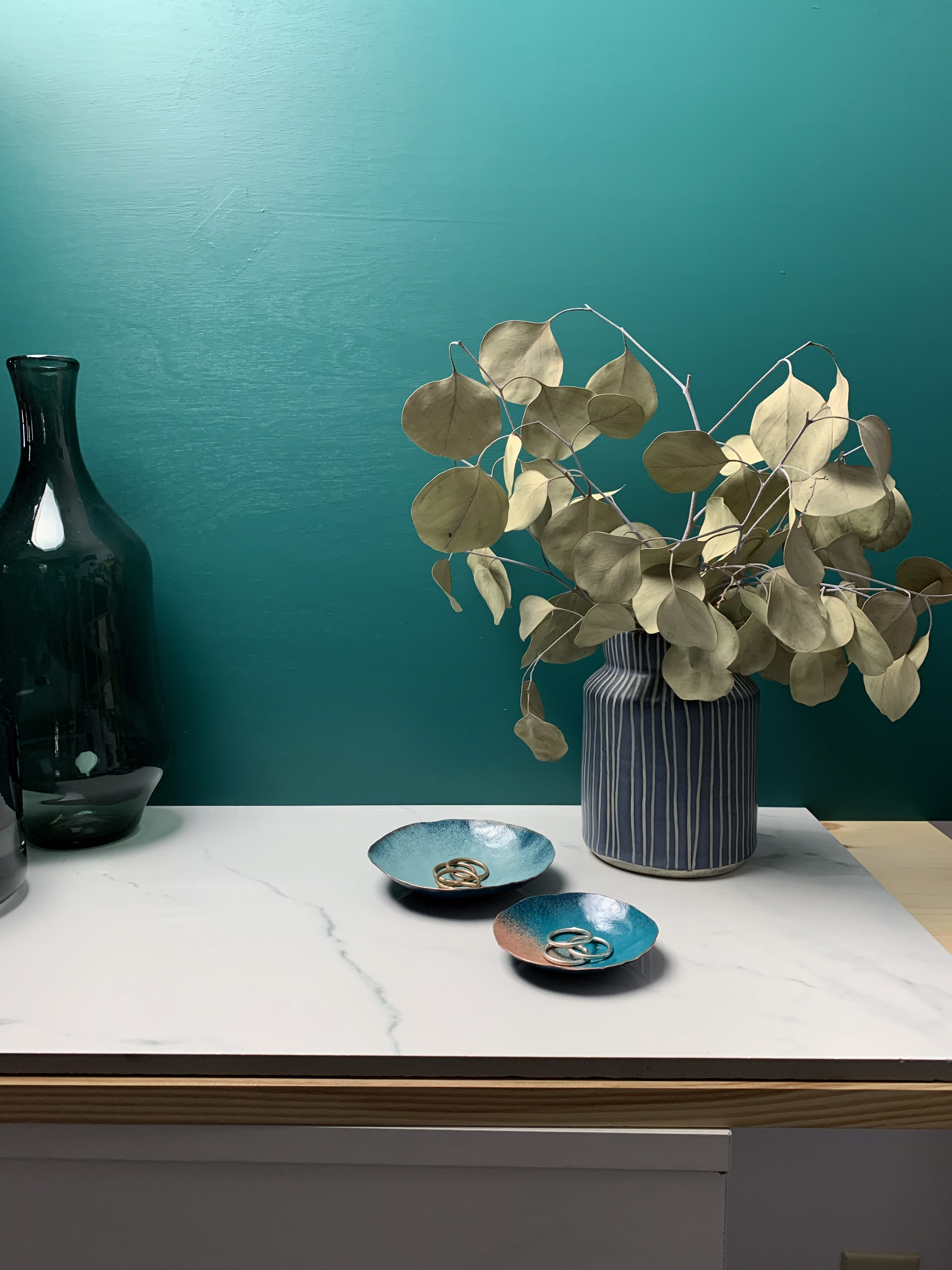 vanity countertop decor with dark teal walls: decorative metal ring dishes and vase with eucalyptus 