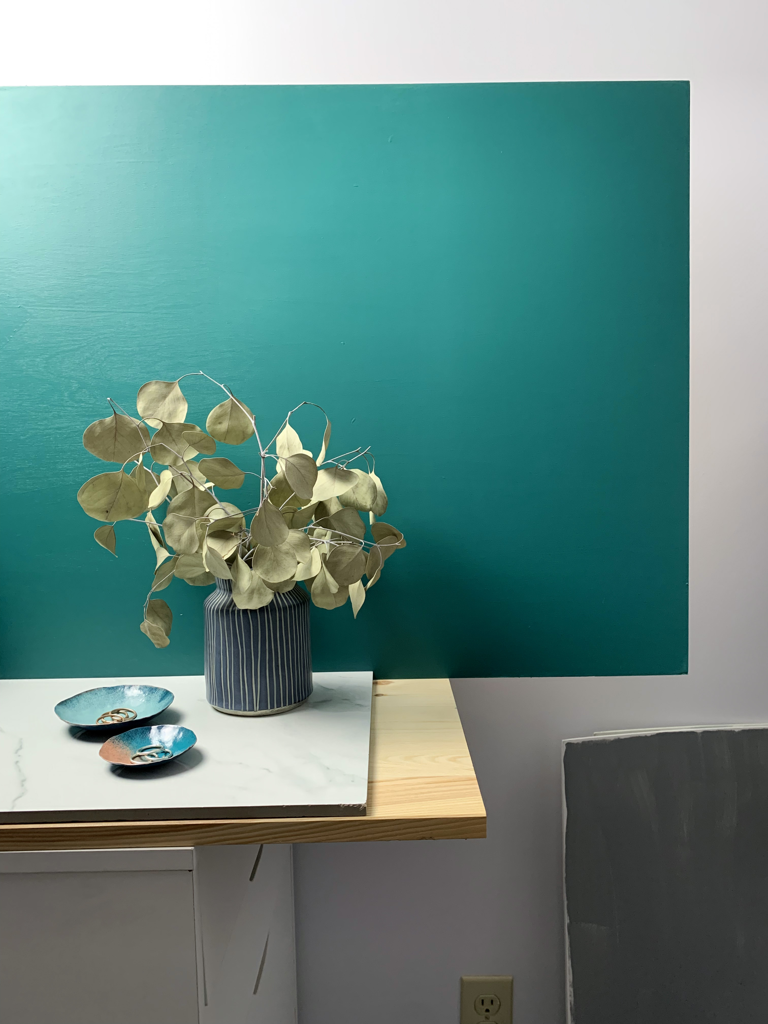 vanity countertop decor with dark teal walls: decorative metal ring dishes and vase with eucalyptus 