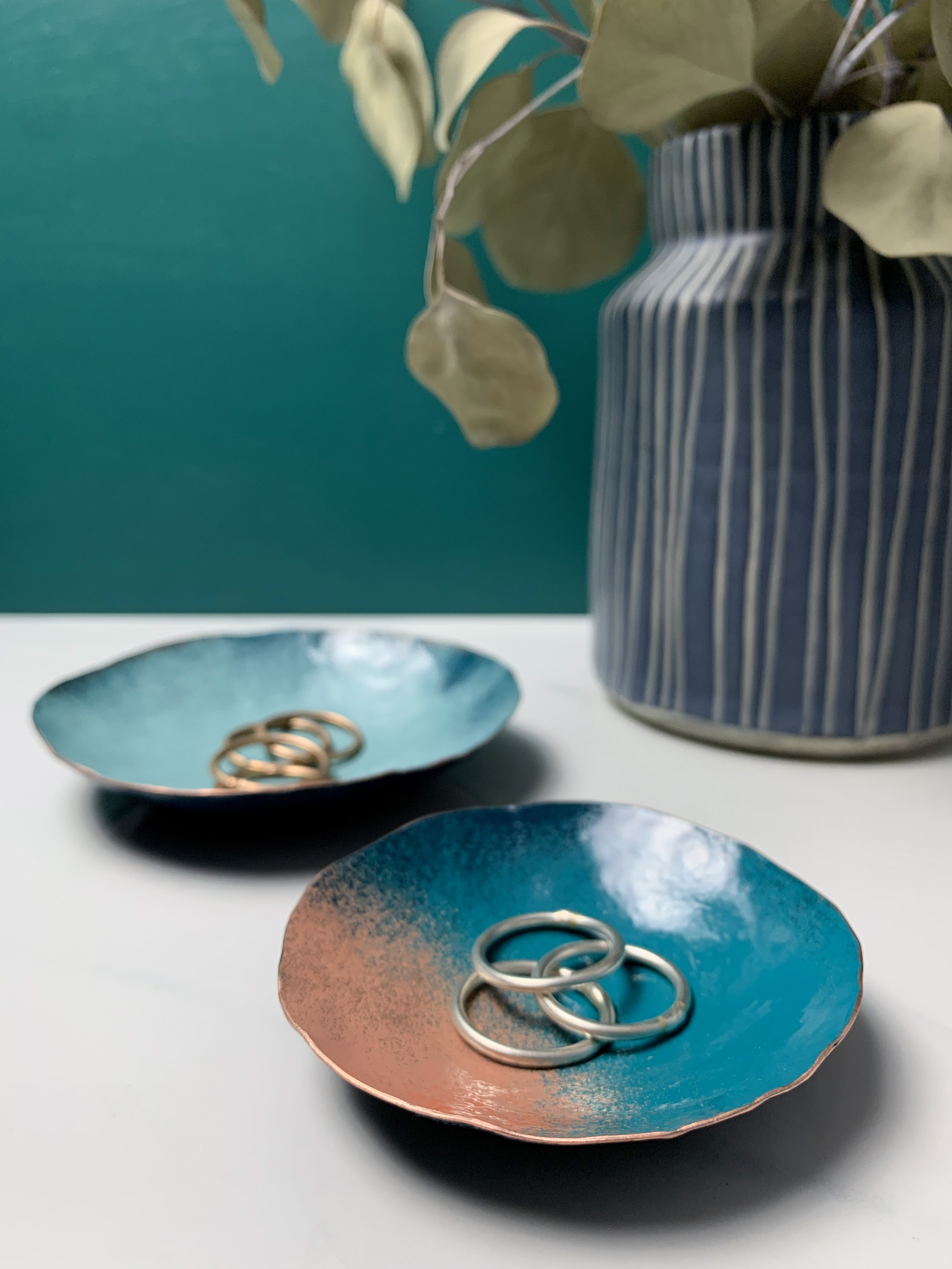 vanity countertop decor with dark teal walls: decorative metal ring dishes and vase with eucalyptus 