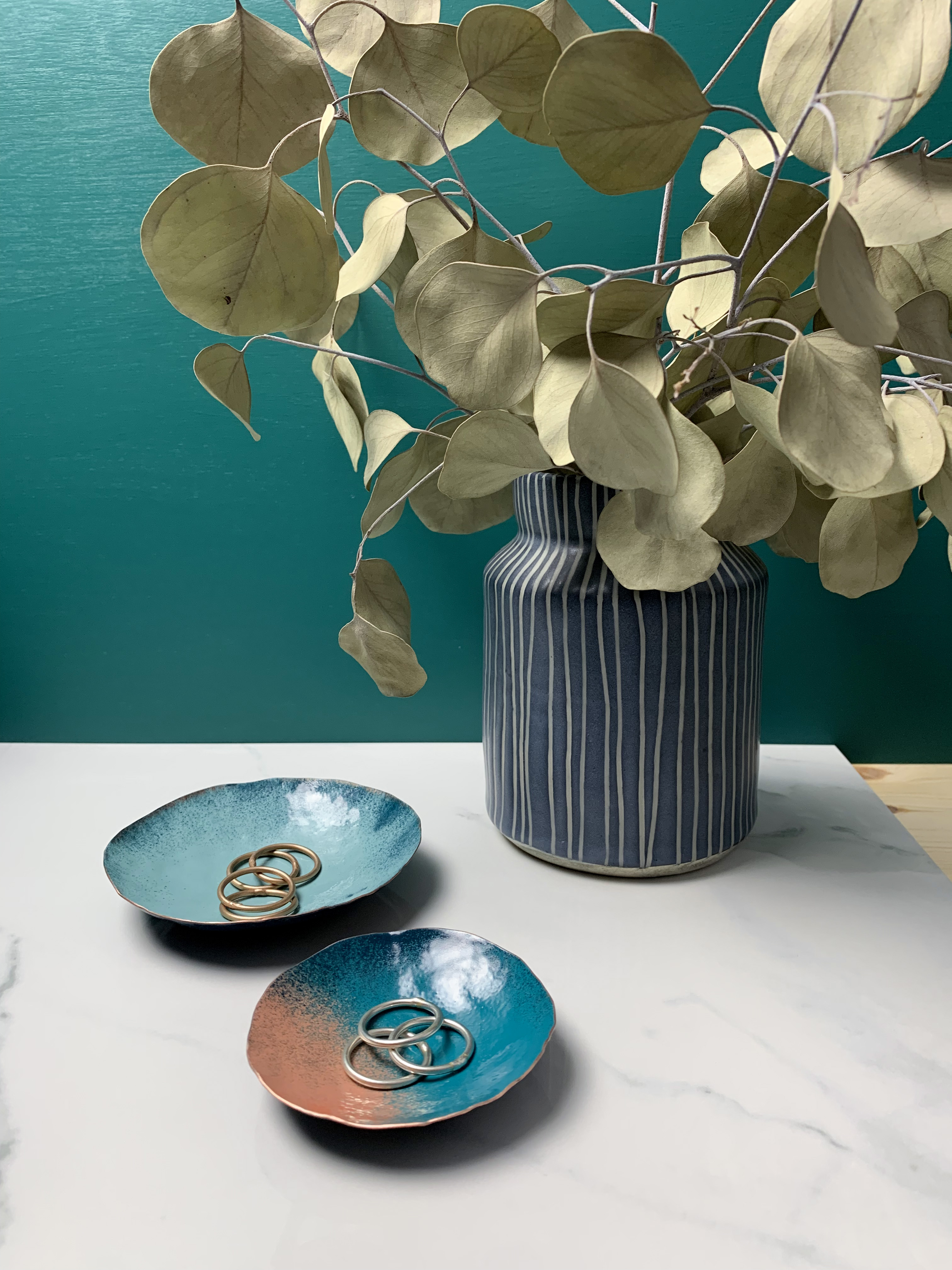 vanity countertop decor with dark teal walls: decorative metal ring dishes and vase with eucalyptus 