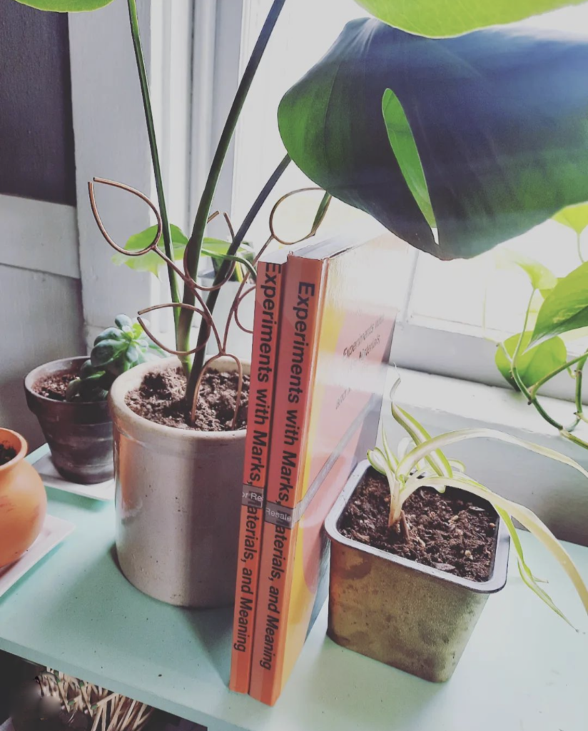 handmade bronze plant stake in monstera deliciosa with art and design books