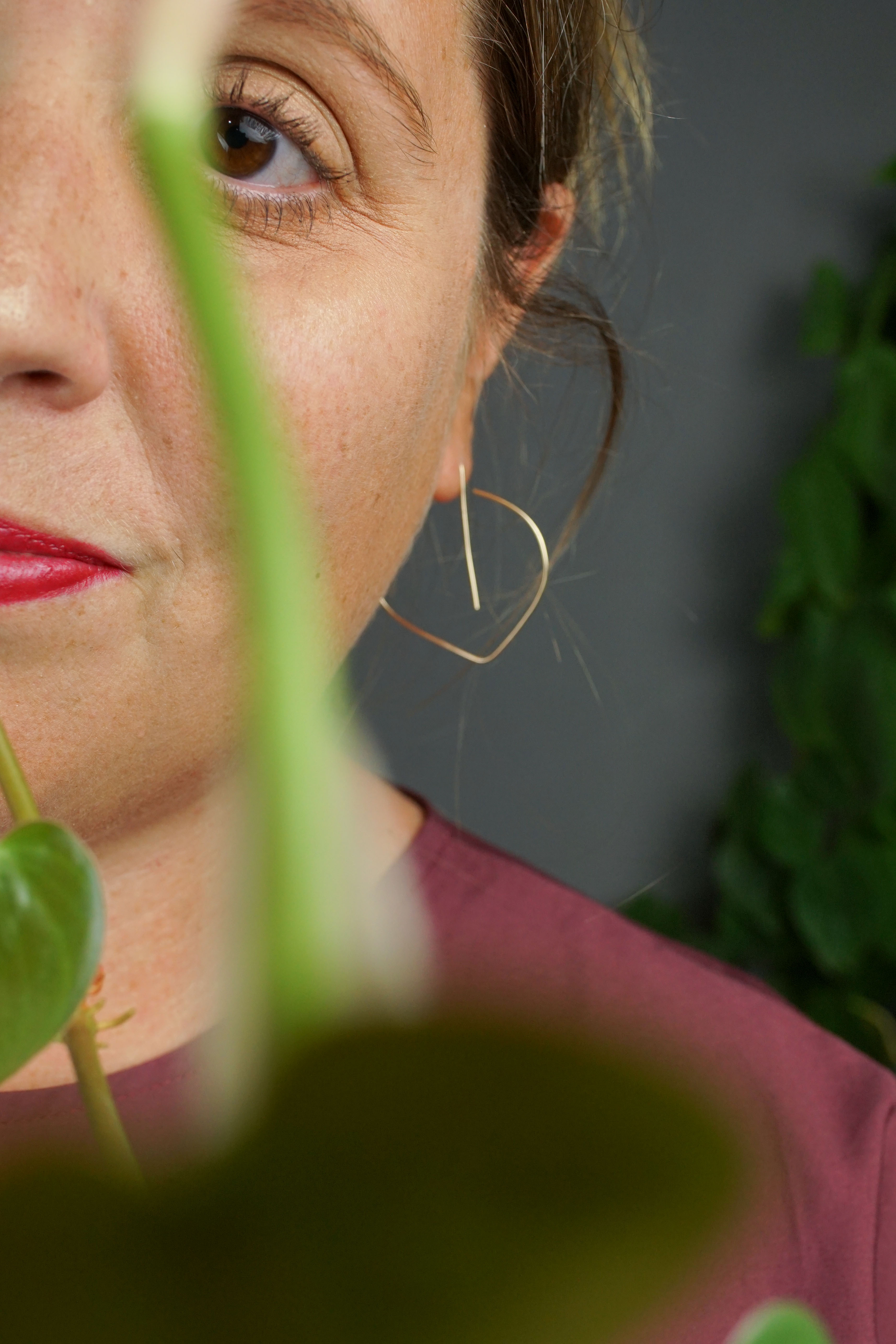woman wearing burgundy dress and gold threader hoop earrings and standing in front of a heart-leaf philodendron