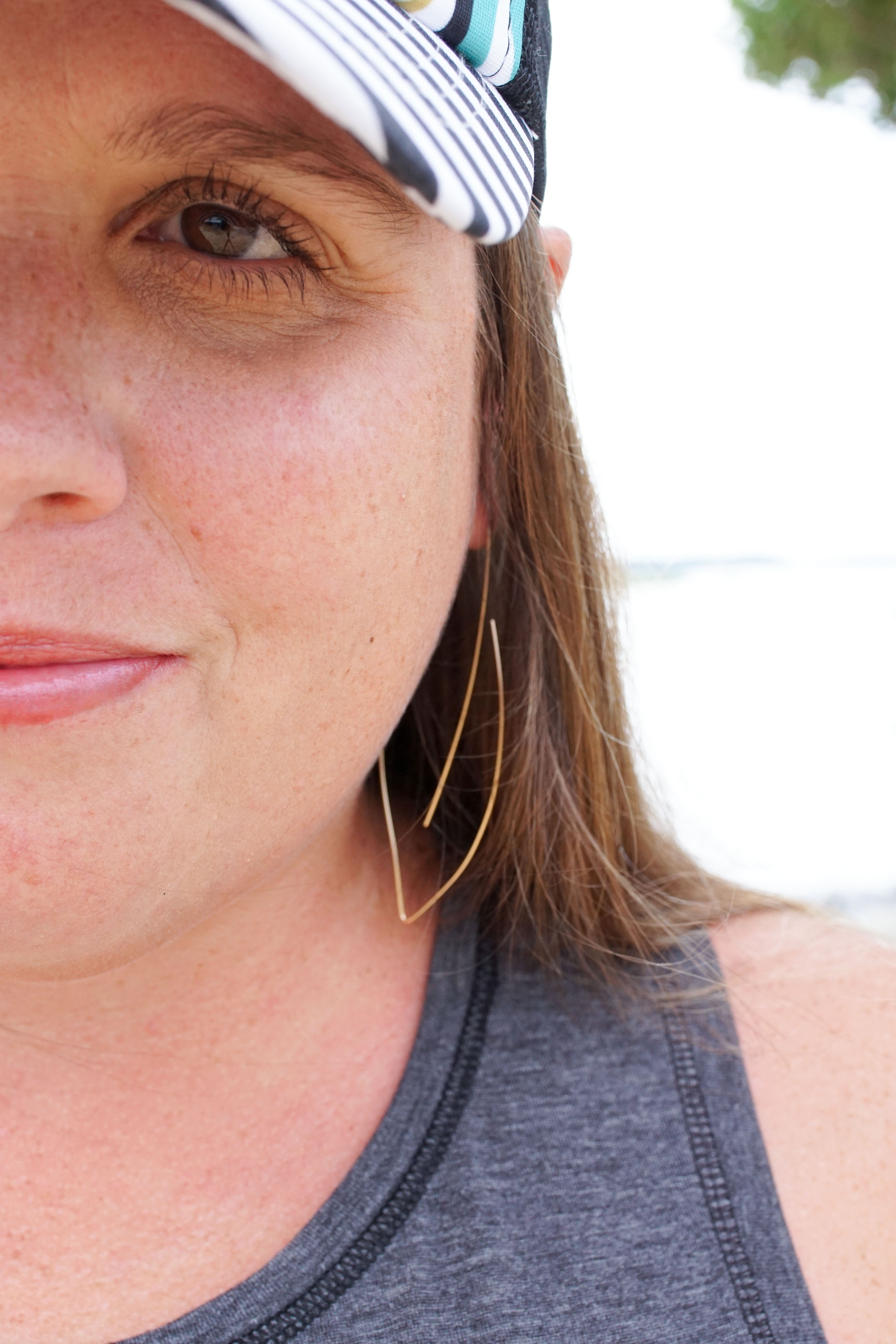 woman wearing gold threader hoop earrings and floral trucker hat at the beach