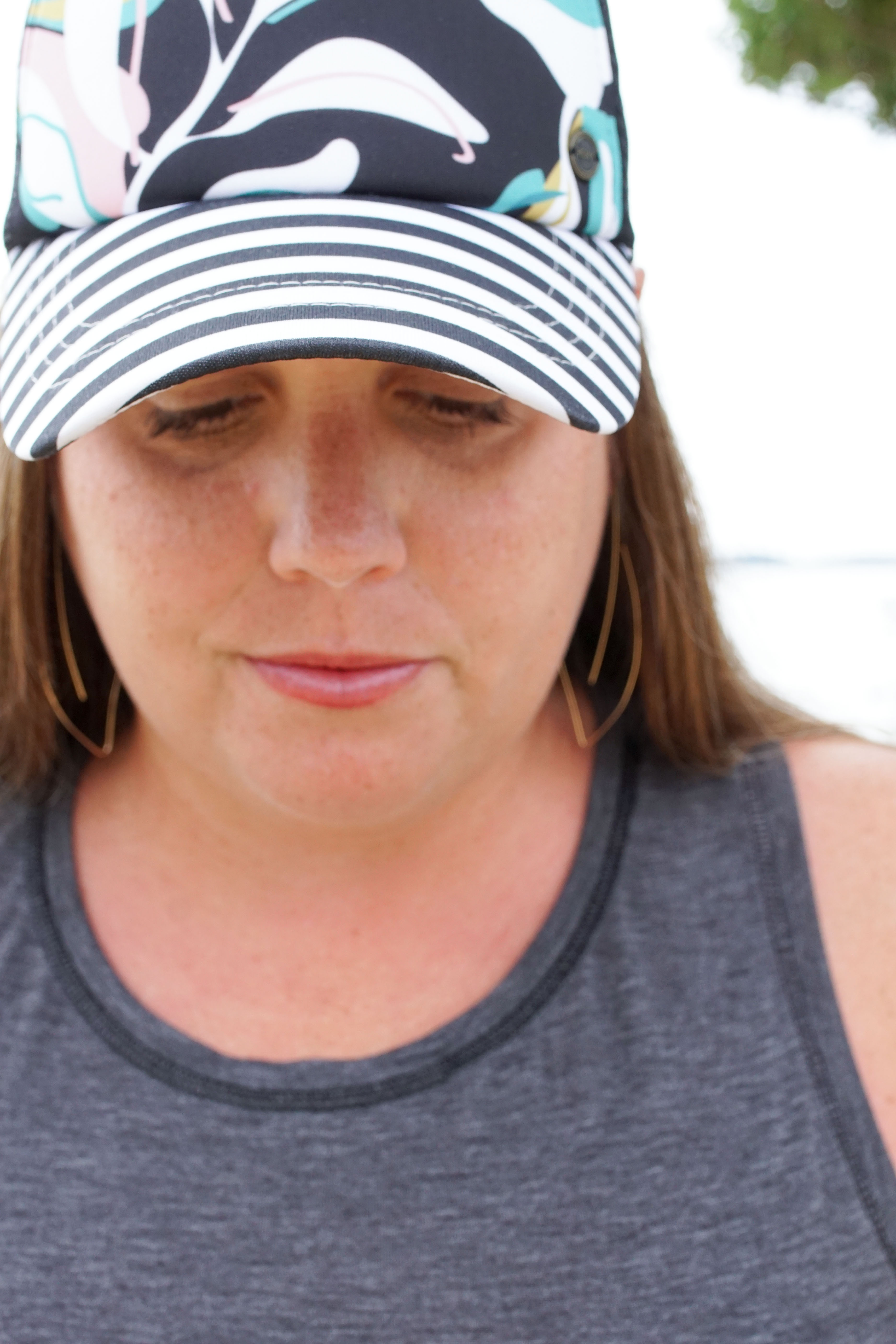 woman wearing gold threader hoop earrings and floral trucker hat at the beach