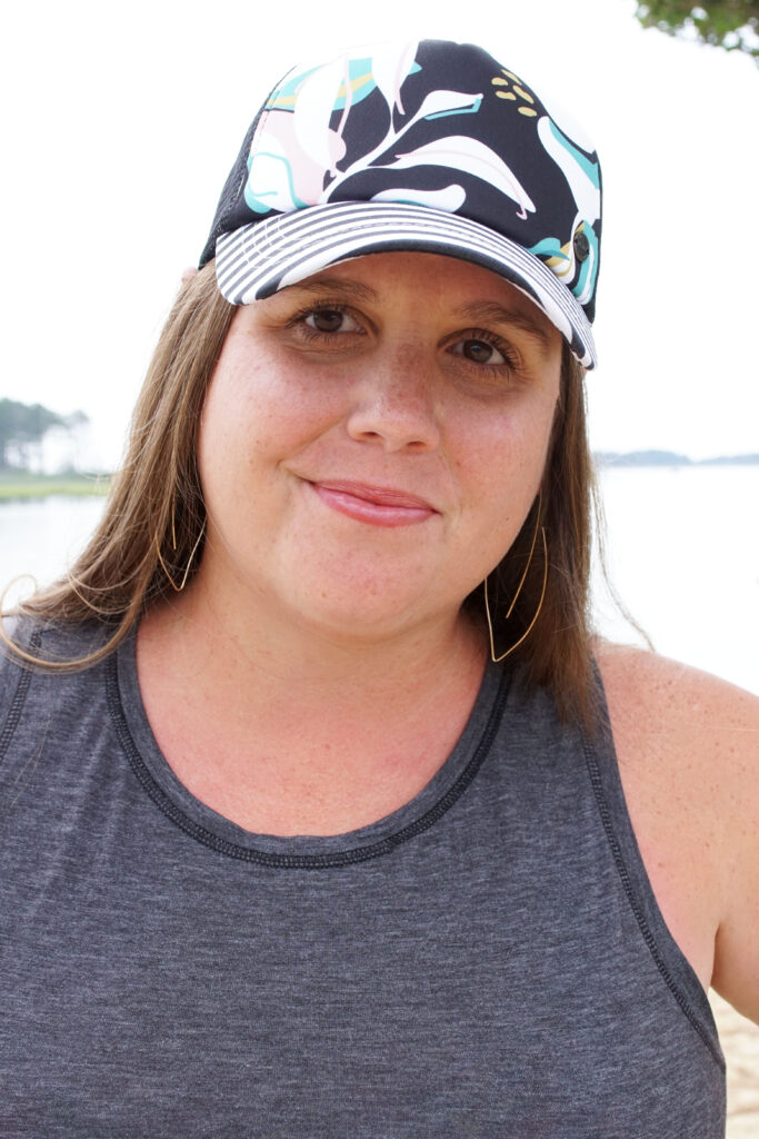 woman wearing gold threader hoop earrings and floral trucker hat at the beach