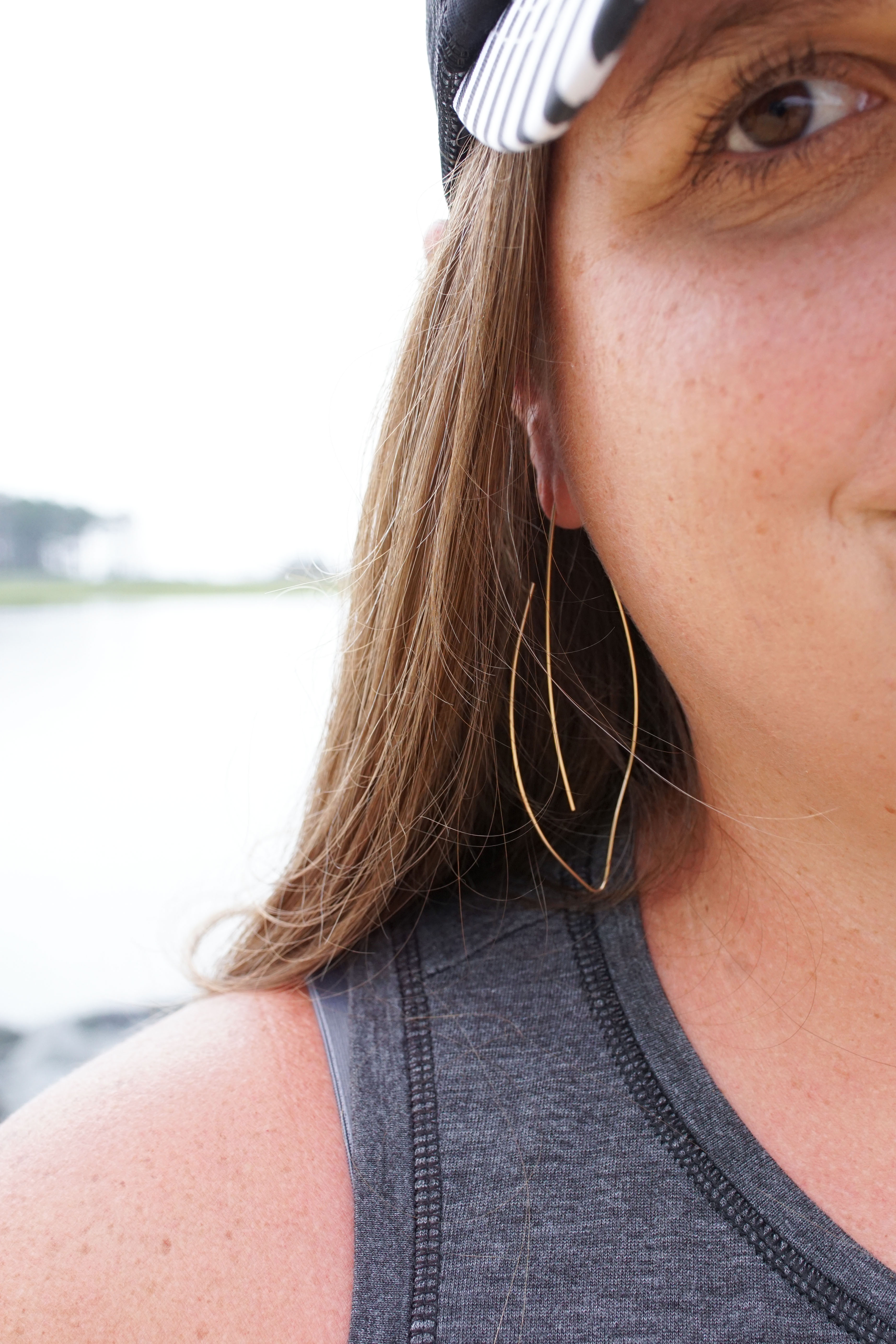 woman wearing gold threader hoop earrings and floral trucker hat at the beach