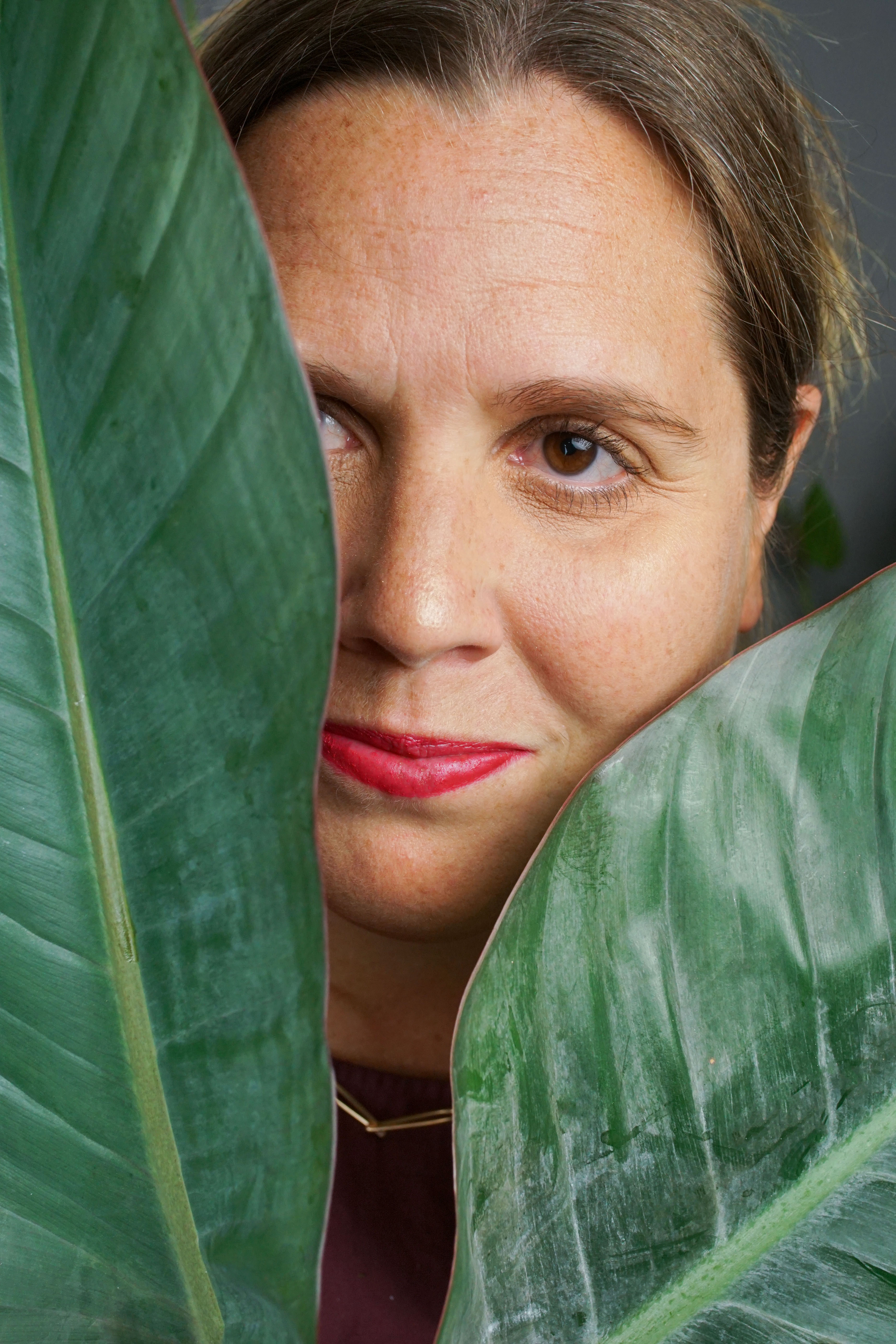 self-portrait of woman wearing bronze chain link necklace behind plant