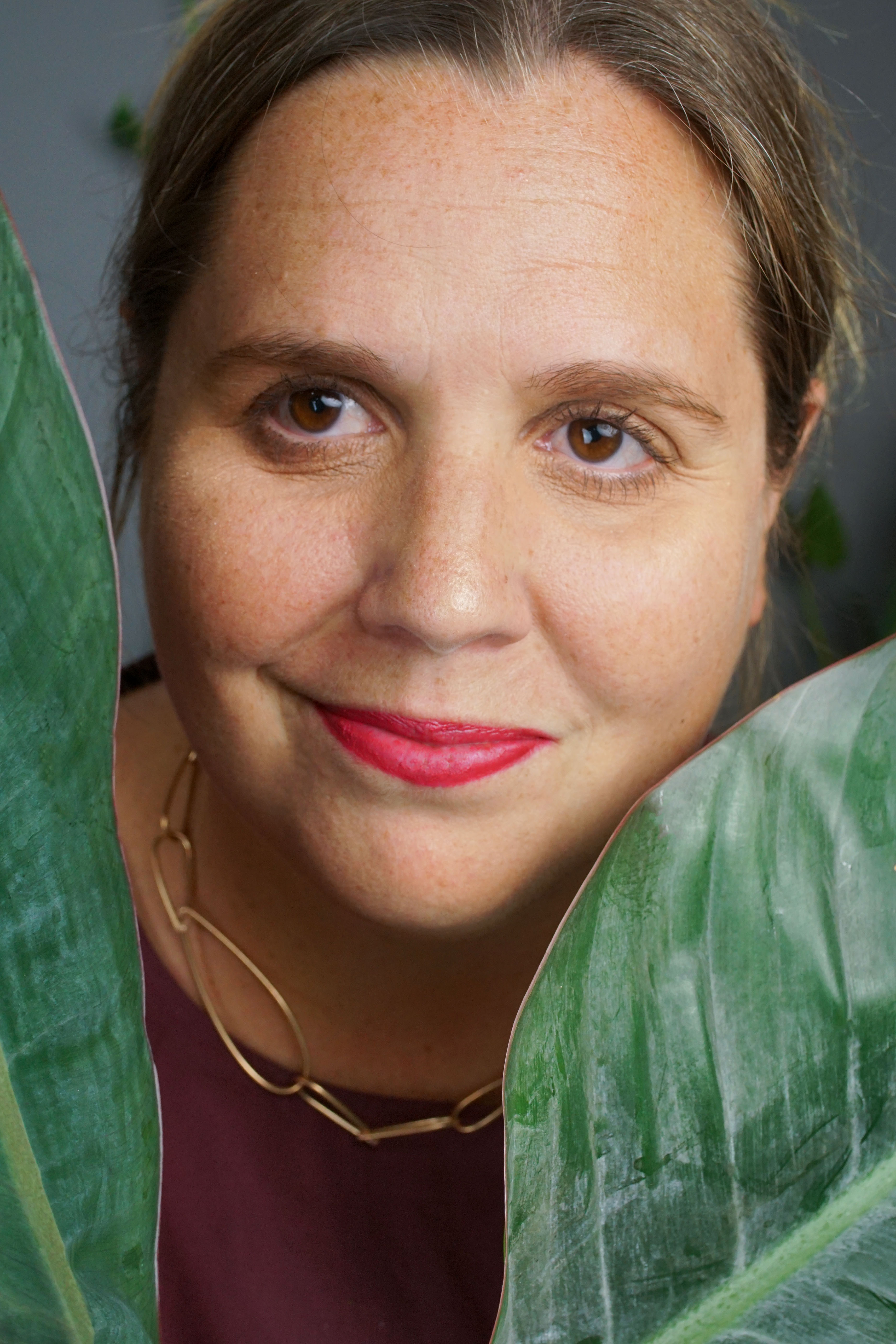 self-portrait of woman wearing bronze chain link necklace behind plant