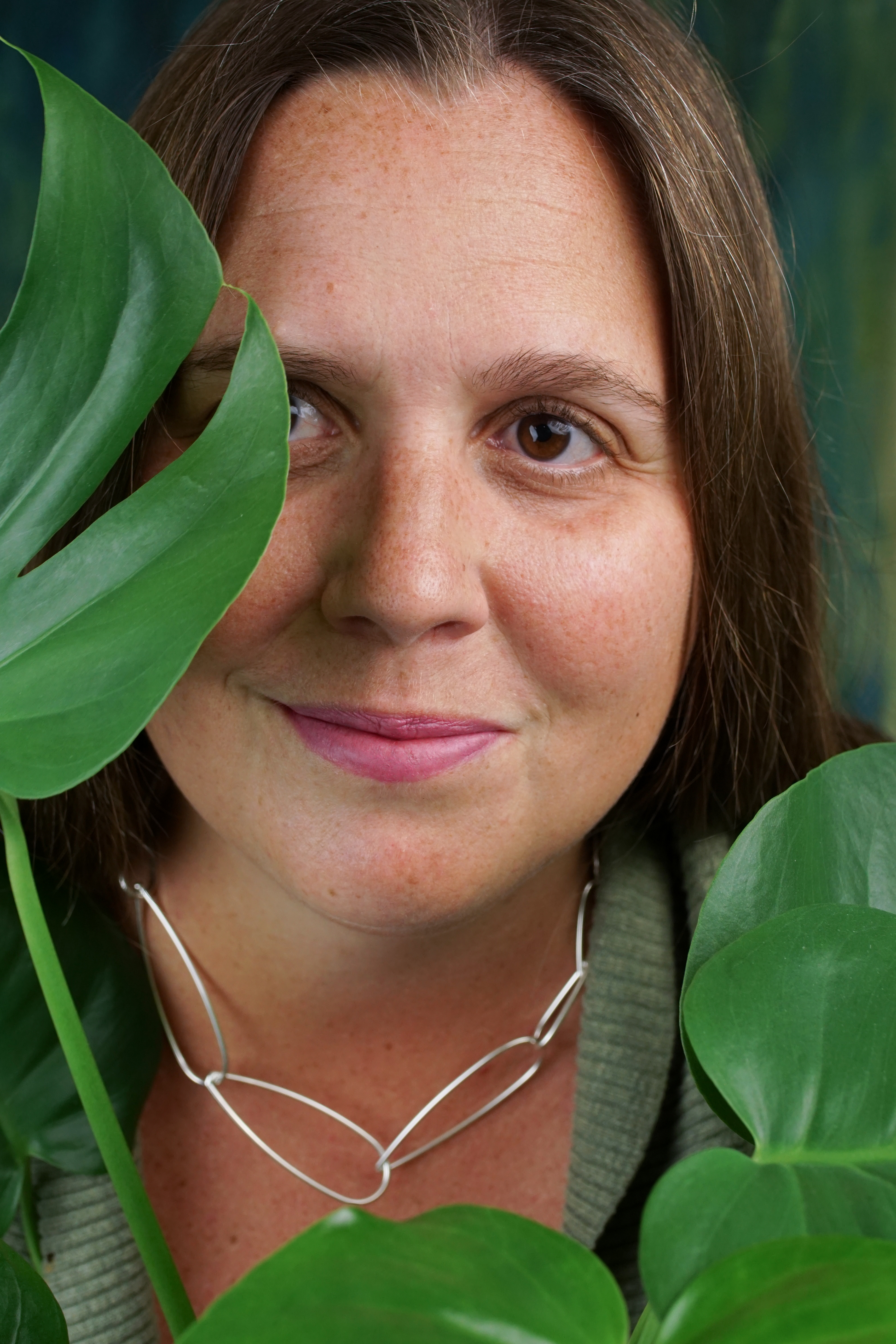 portrait of a woman wearing no makeup behind a monstera house plant