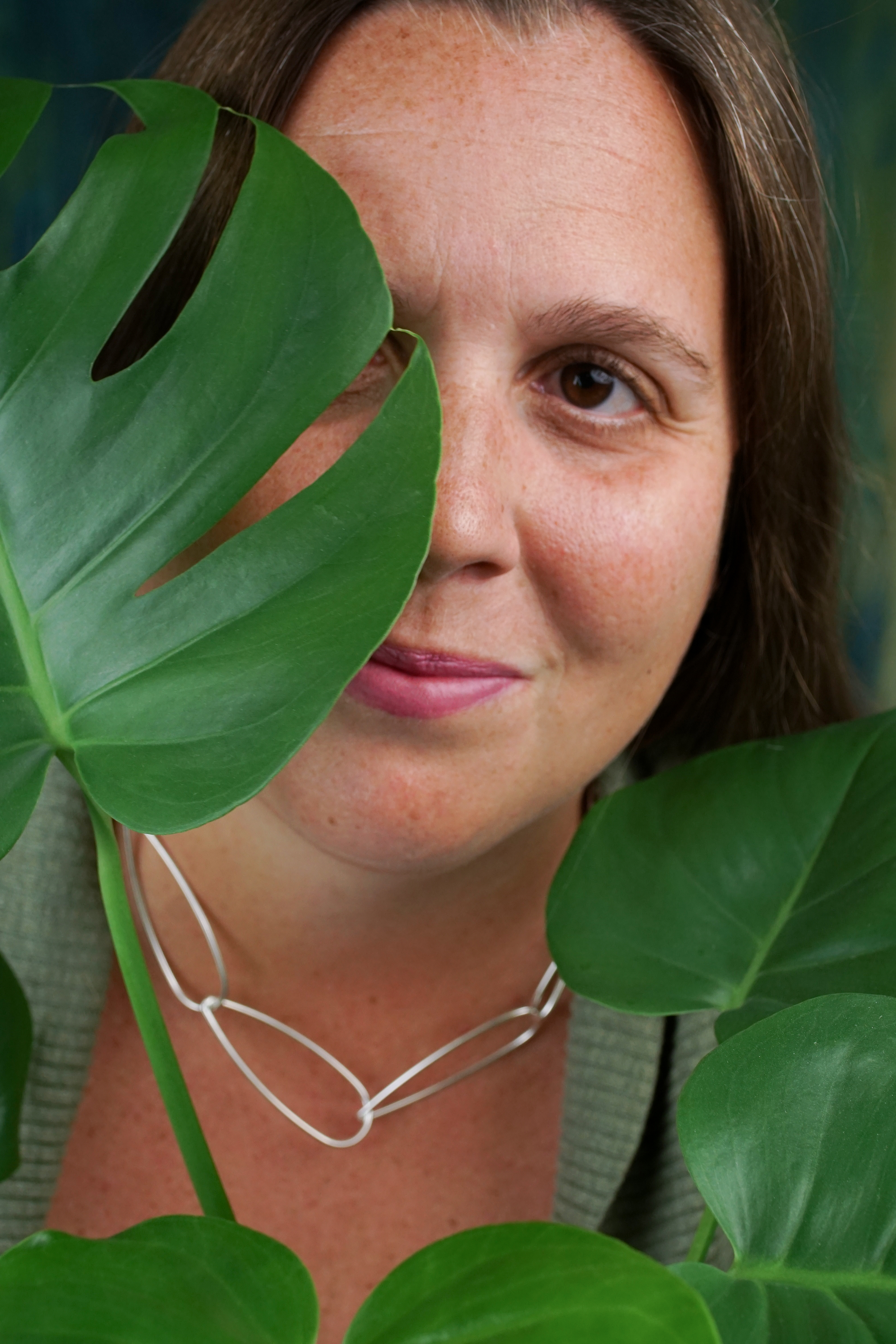 portrait of a woman wearing no makeup behind a monstera house plant