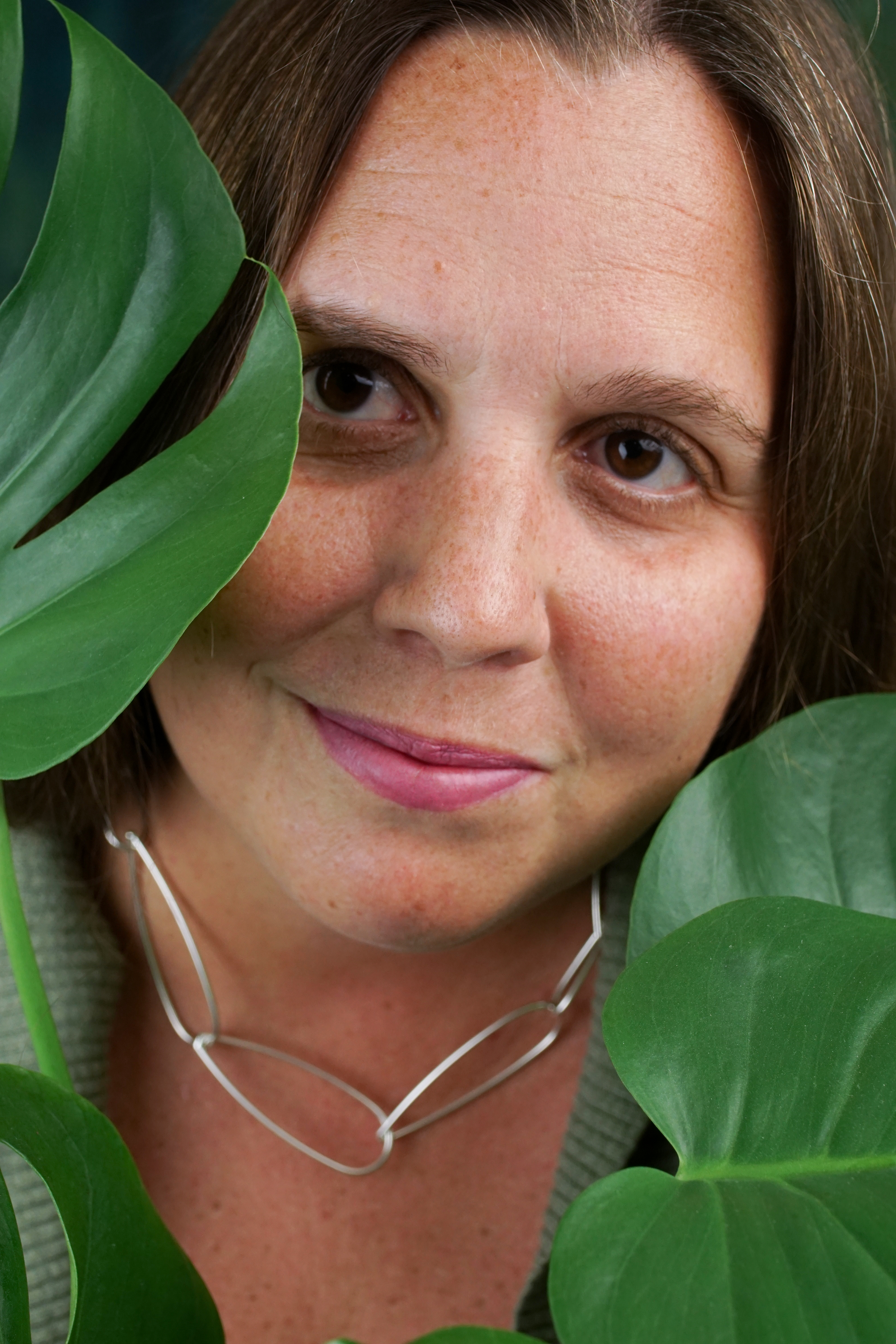 portrait of a woman wearing no makeup behind a monstera house plant