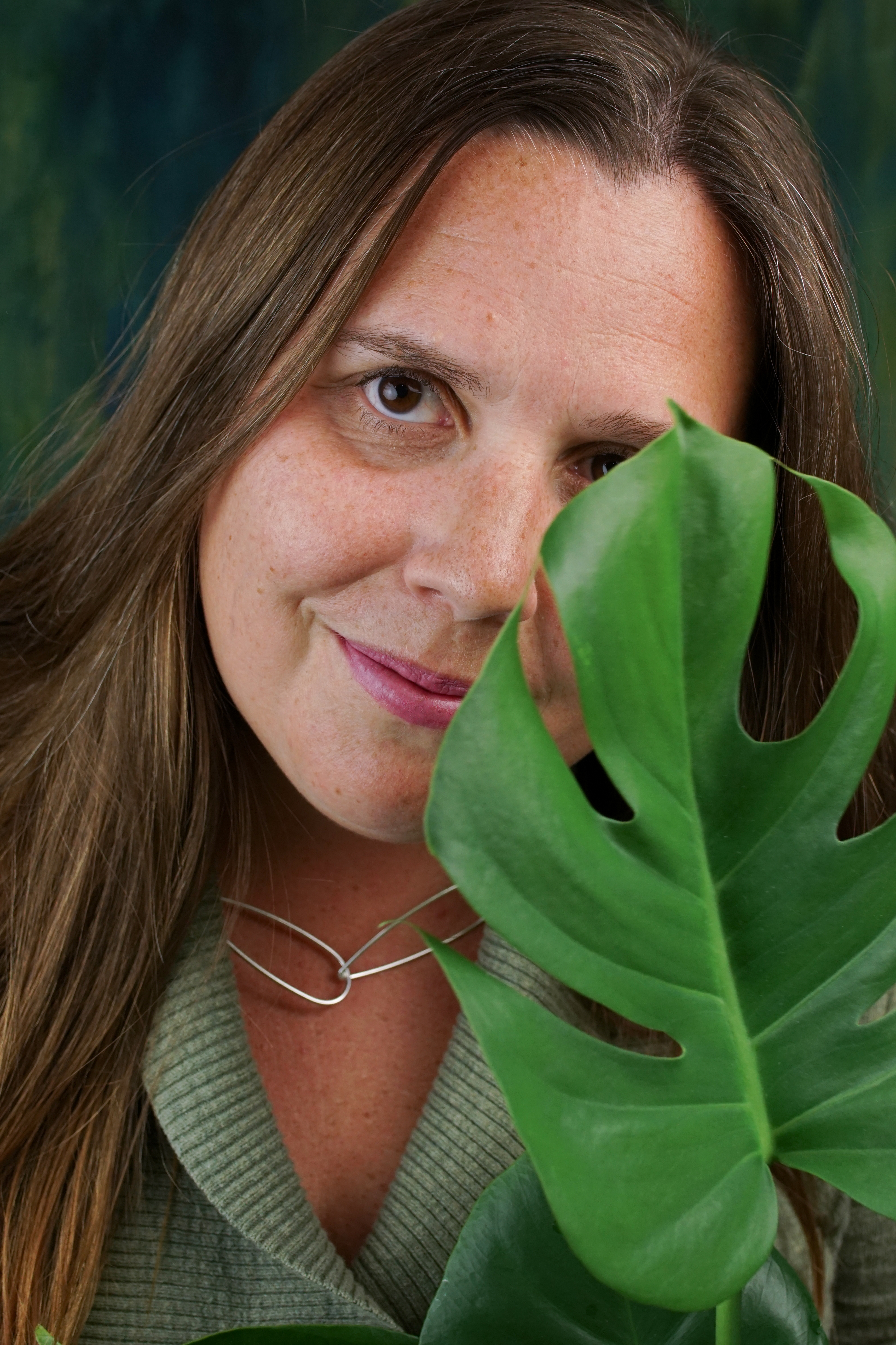 portrait of a woman wearing no makeup behind a monstera house plant