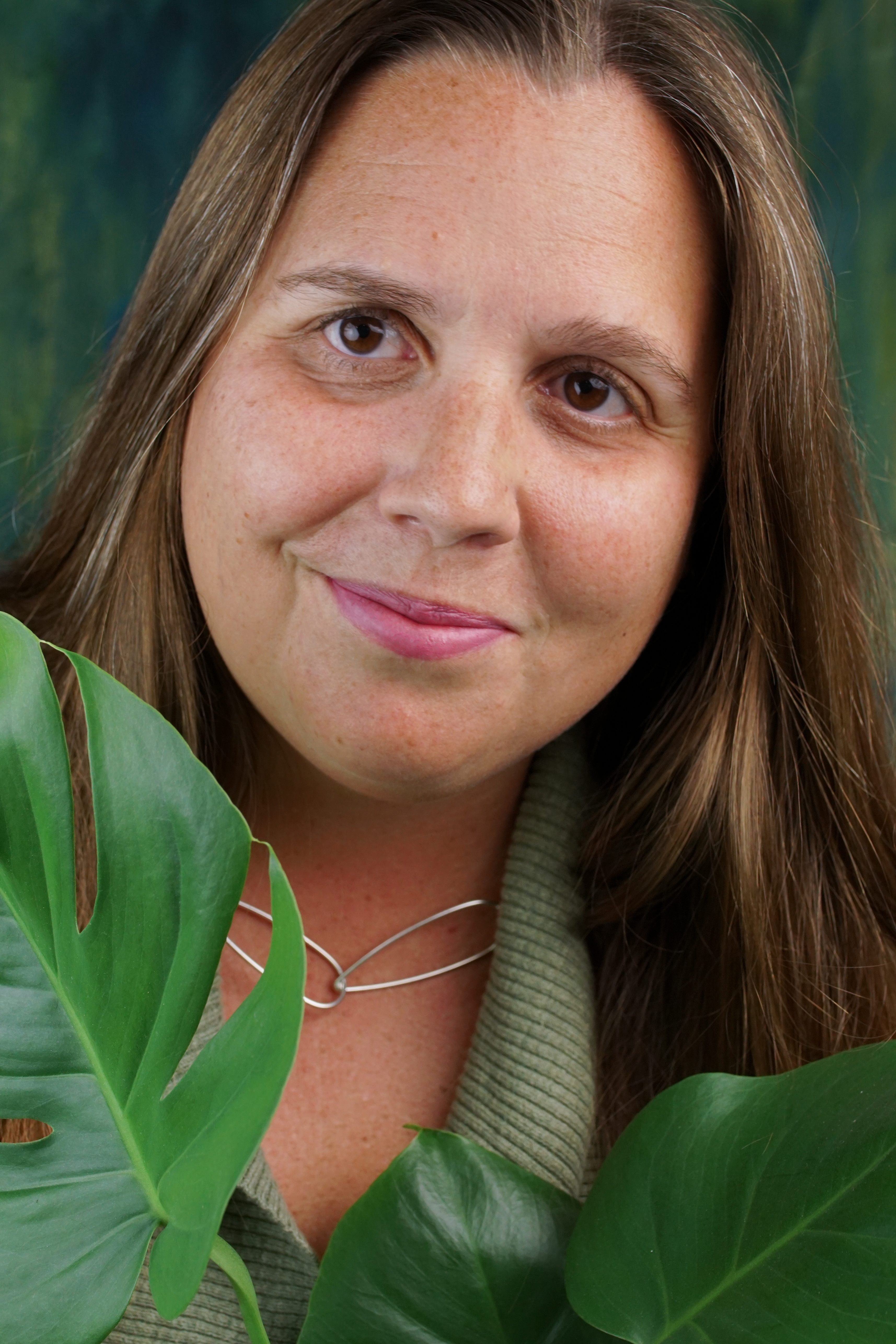 portrait of a woman wearing no makeup behind a monstera house plant
