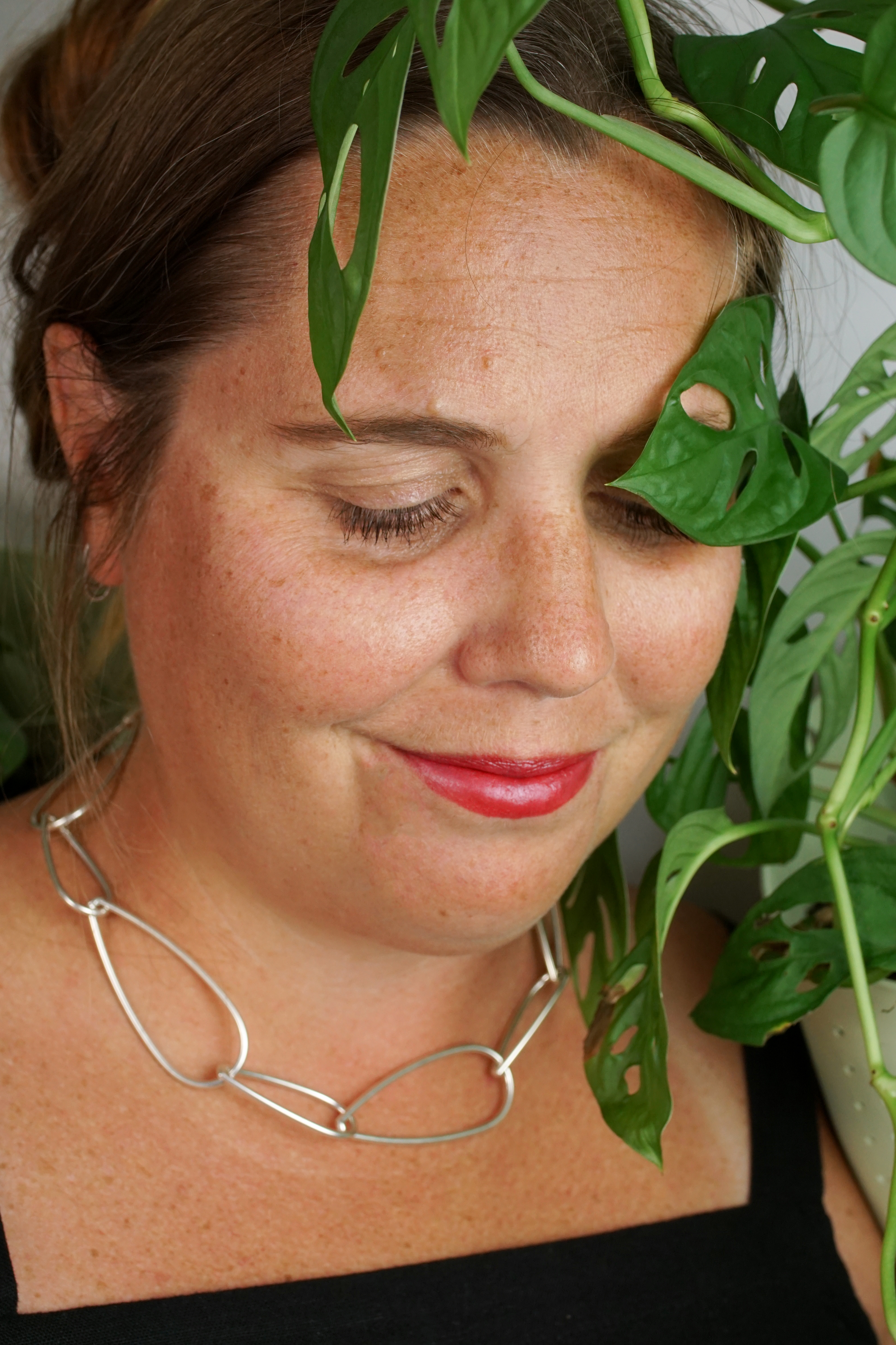 woman wearing silver chain necklace and standing next to monstera adonsonii house plant