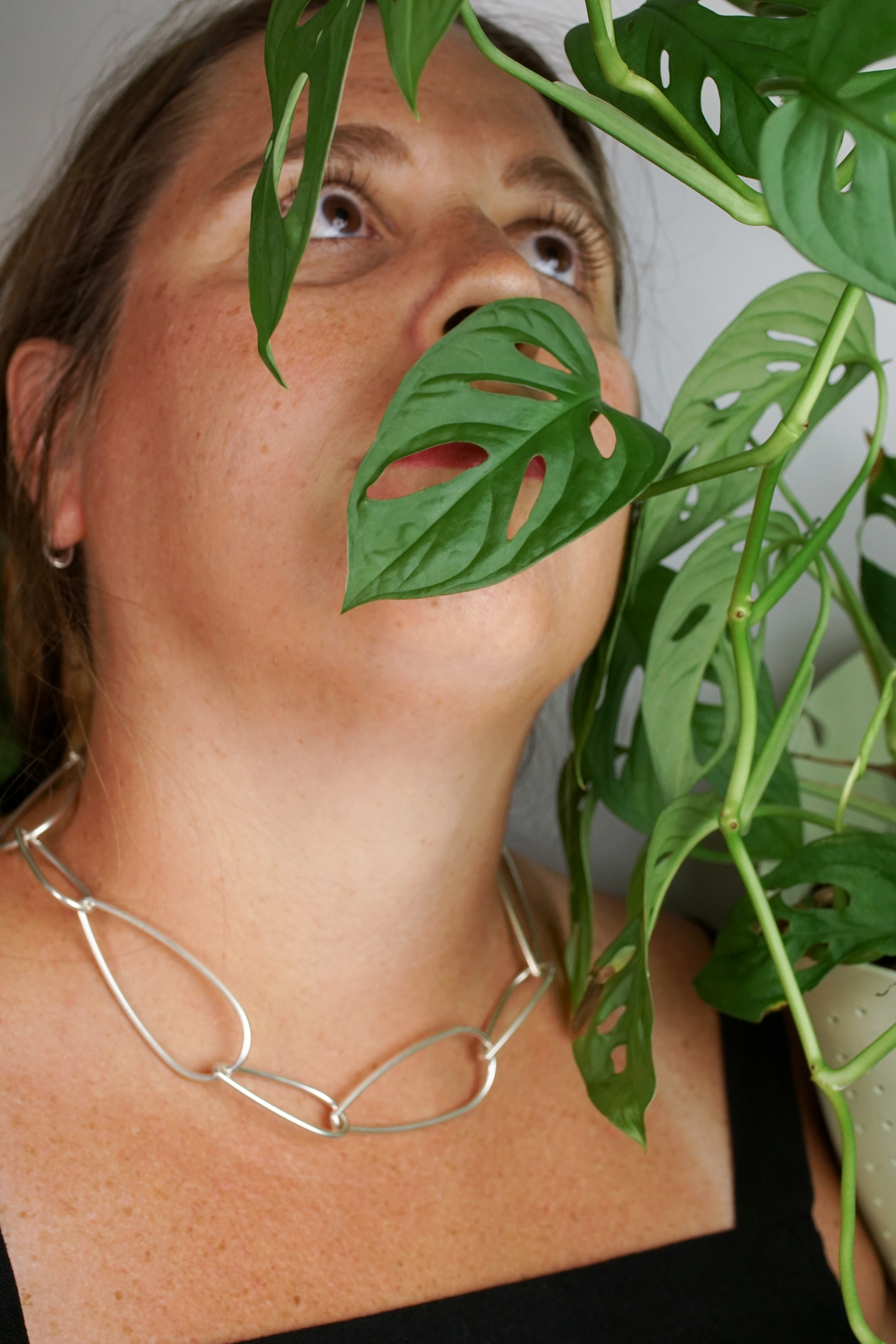 woman wearing silver chain necklace and standing next to monstera adonsonii house plant