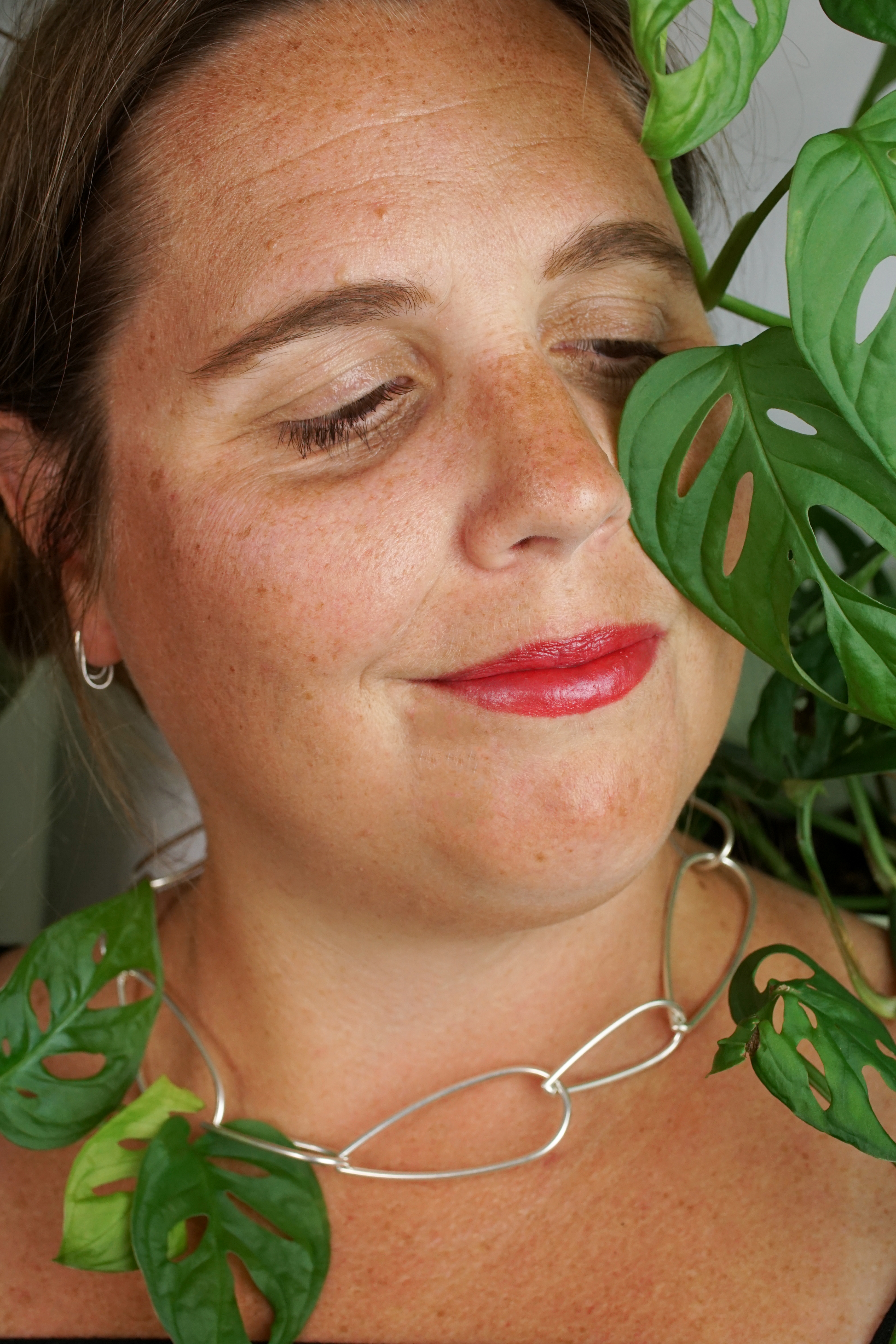 woman wearing silver chain necklace and standing next to monstera adonsonii house plant