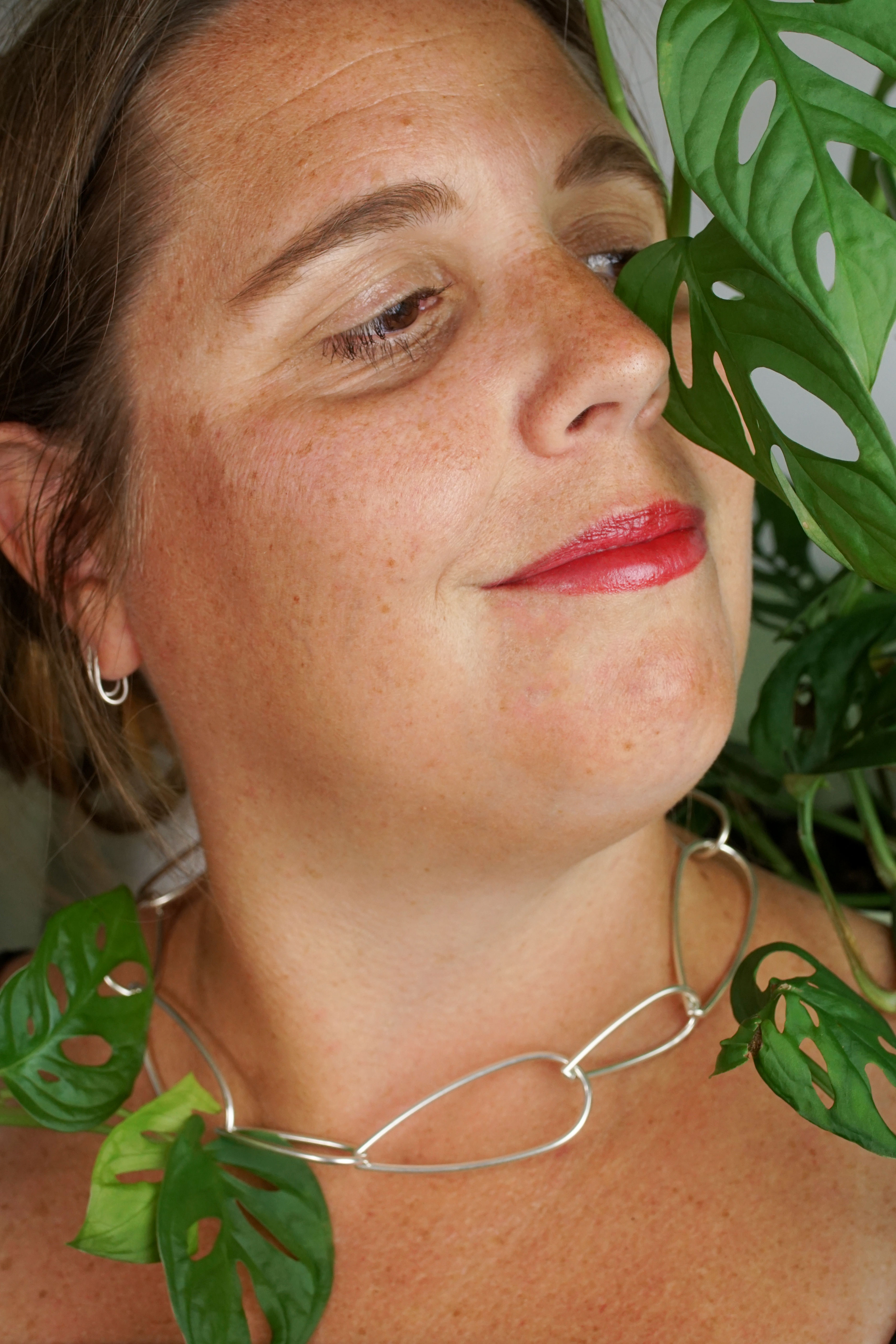 woman wearing silver chain necklace and standing next to monstera adonsonii house plant