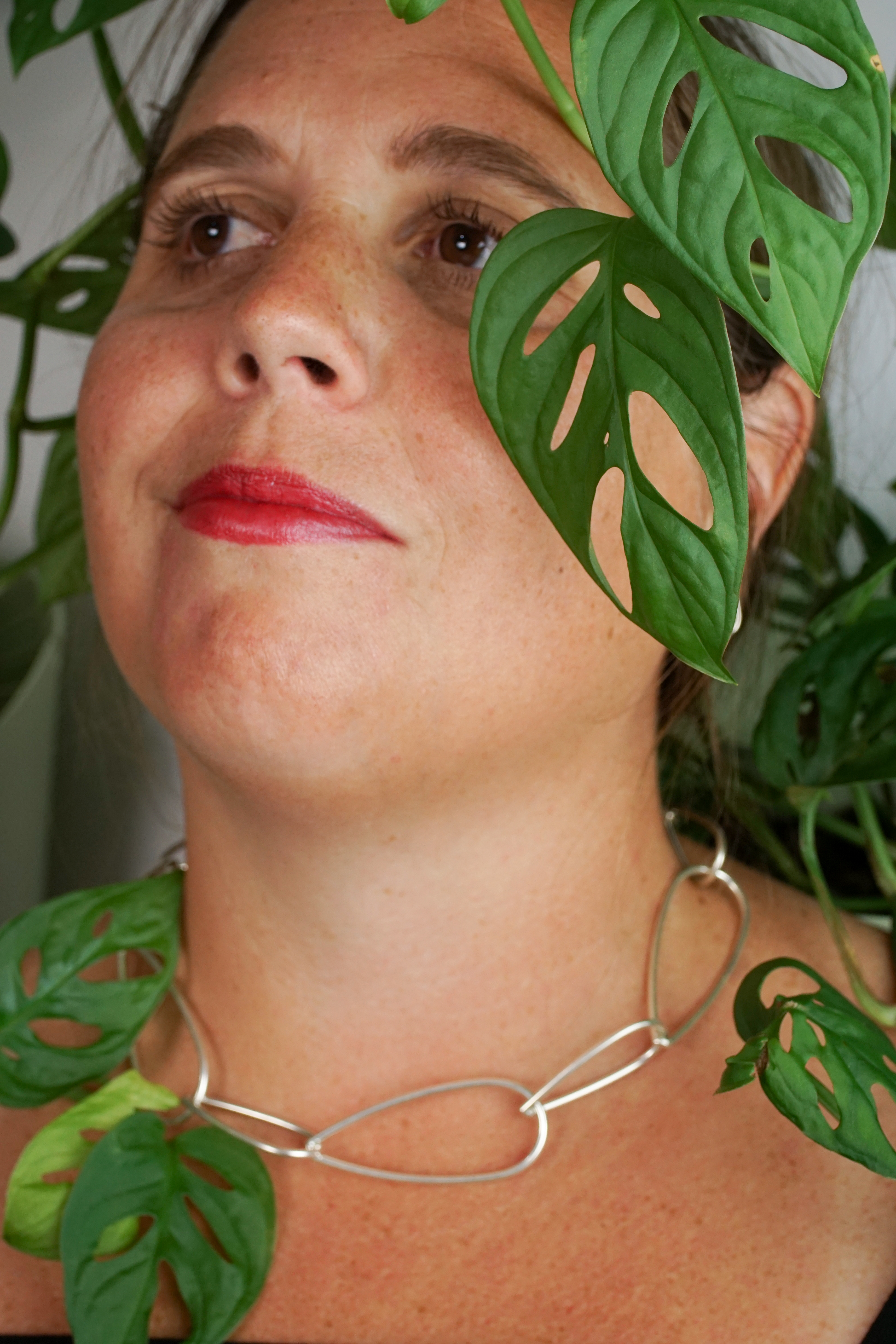woman wearing silver chain necklace and standing next to monstera adonsonii house plant