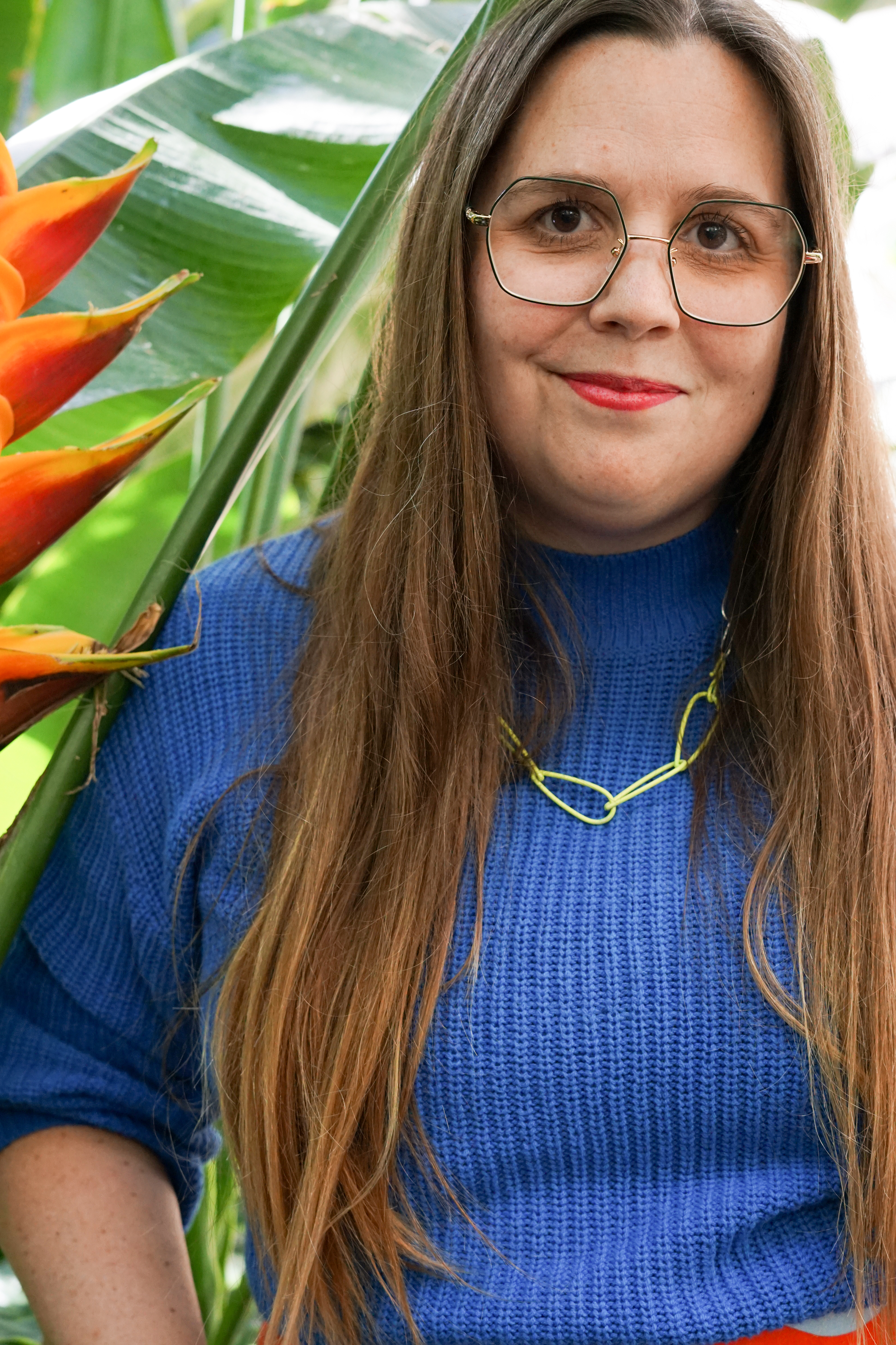 self-portrait in garden with bird of paradise plant, neon necklace, blue sweater, and marimekko skirt