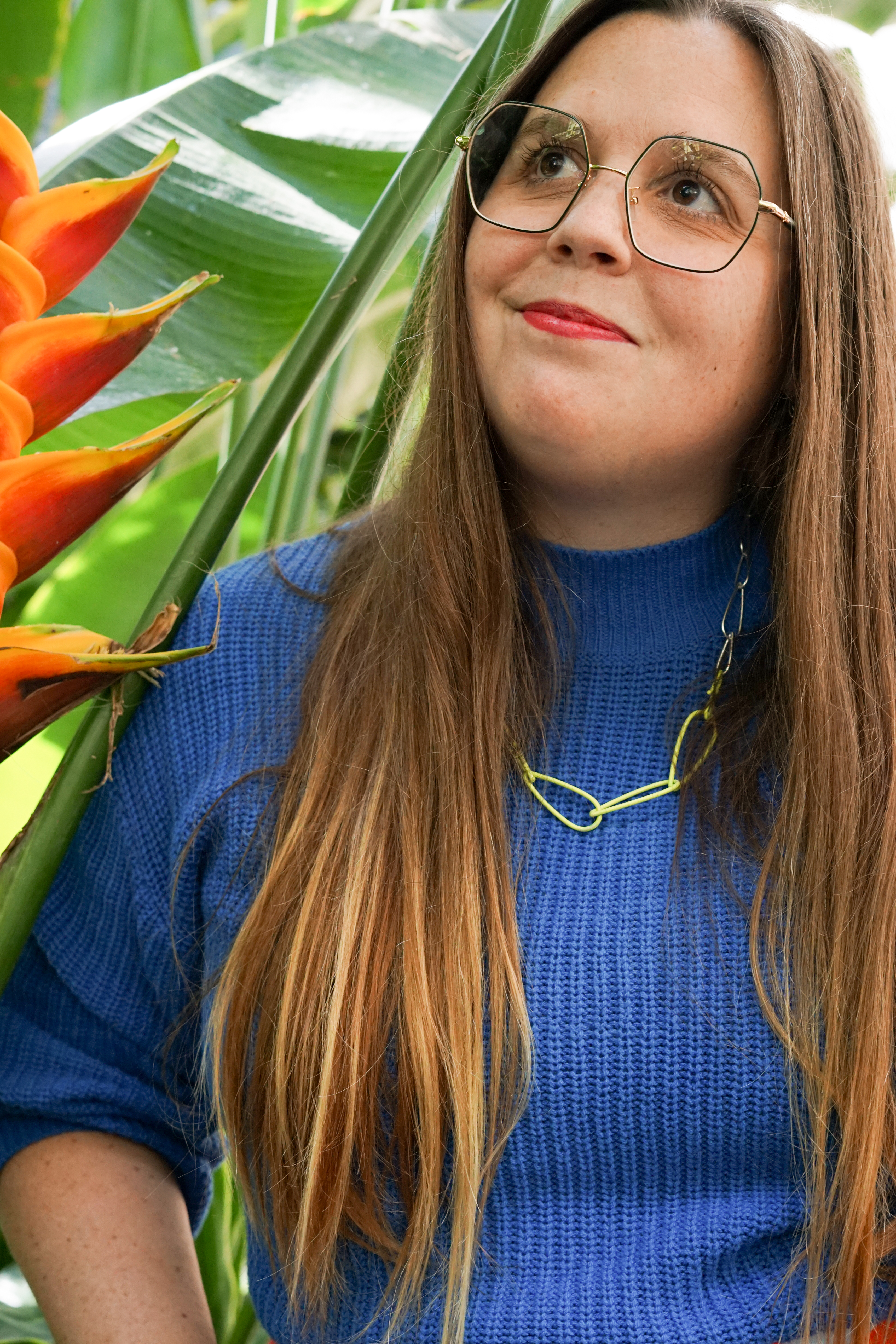 self-portrait in garden with bird of paradise plant, neon necklace, blue sweater, and marimekko skirt