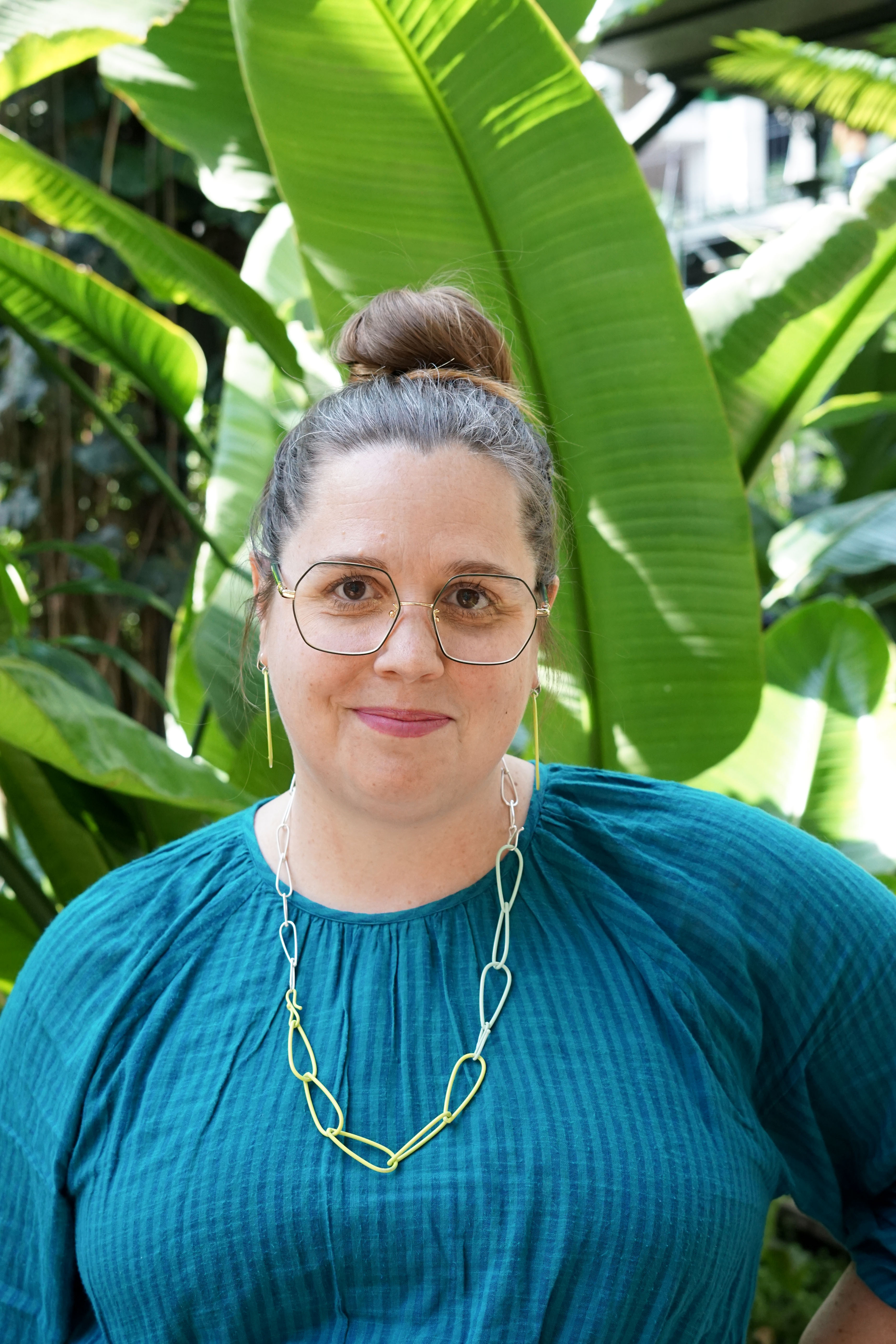 megan in garden with bright green plants, jewelry, and glasses and a teal dress