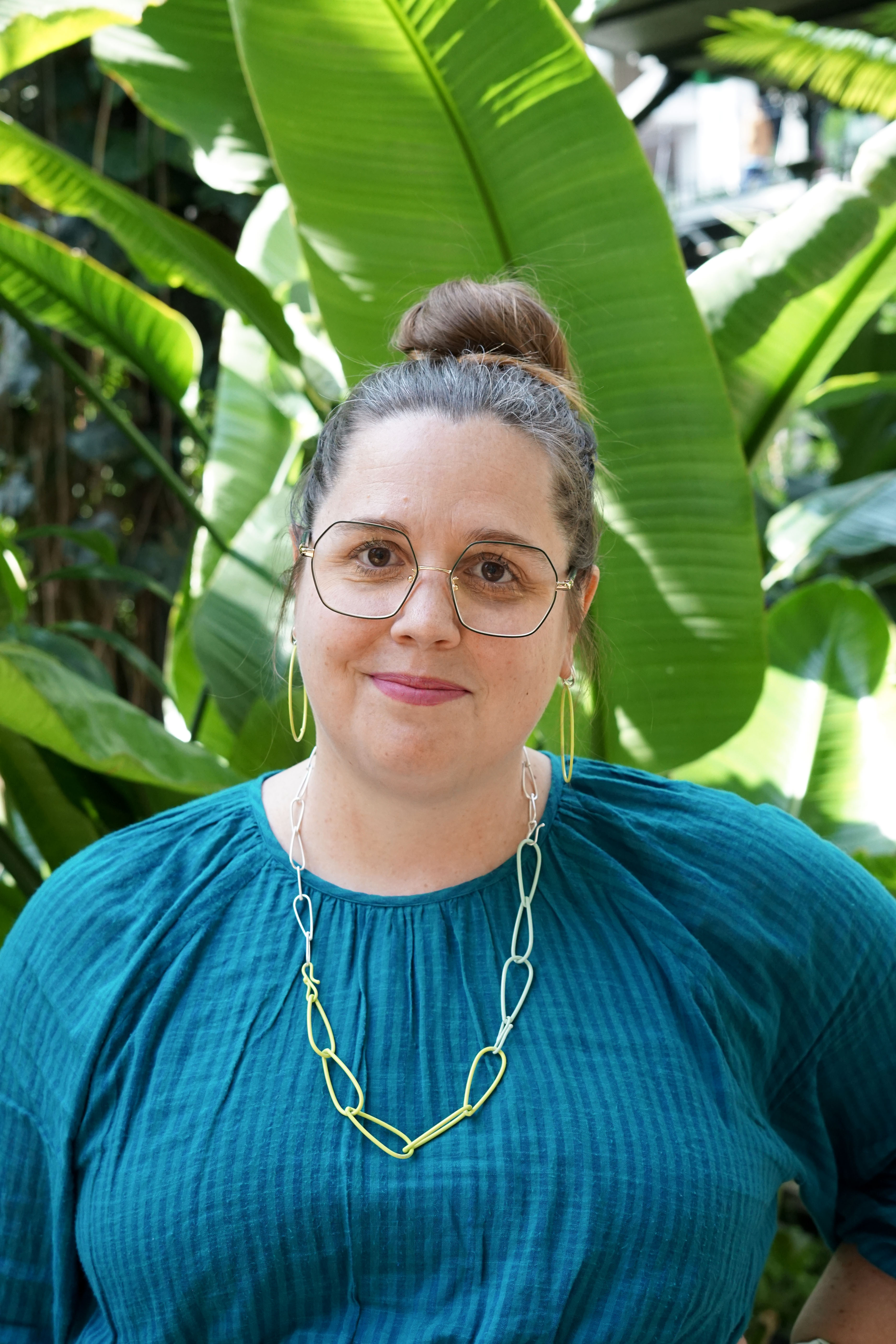 megan in garden with bright green plants, jewelry, and glasses and a teal dress