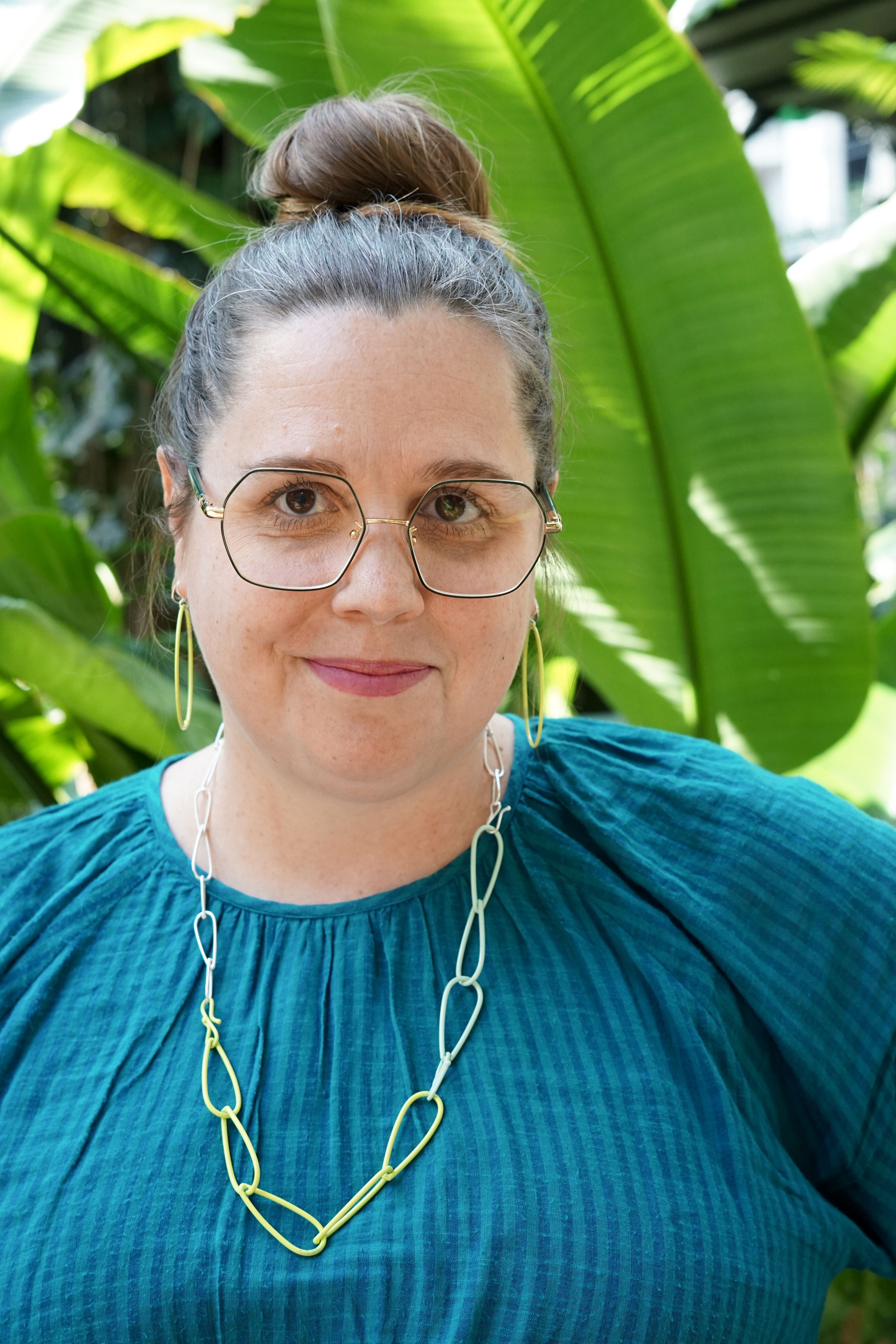 megan in garden with bright green plants, jewelry, and glasses and a teal dress