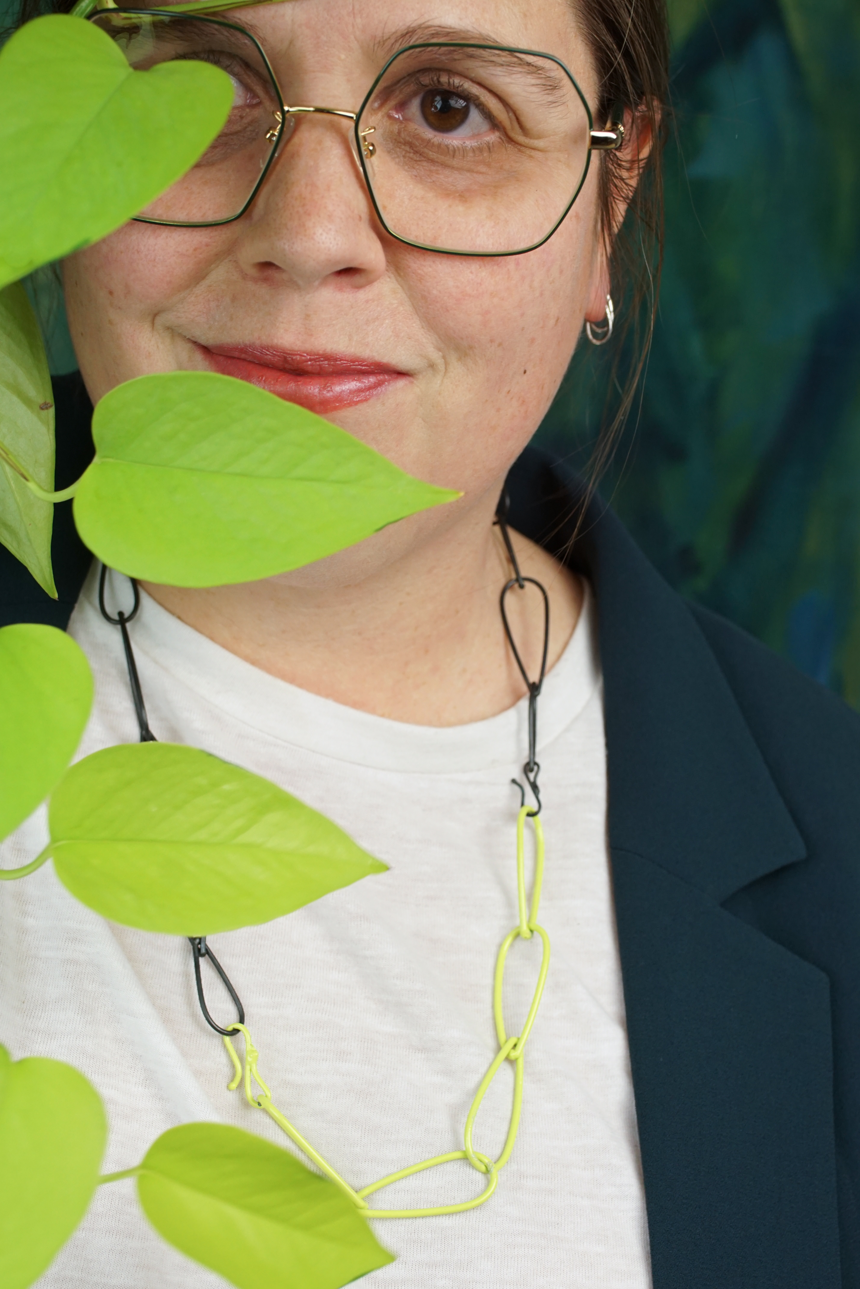 megan wearing green glasses with neon and steel chain necklace and neon pothos plant