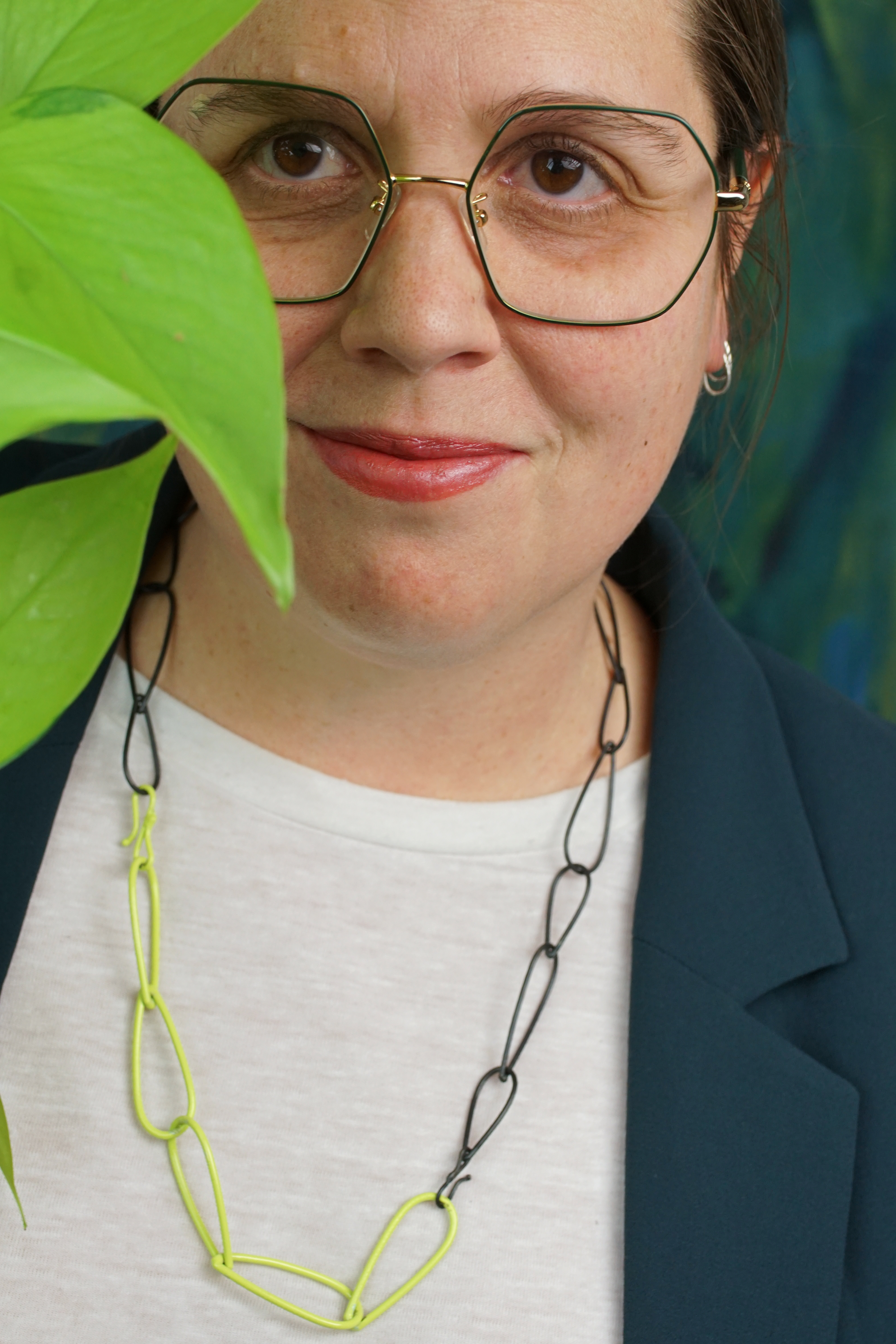megan wearing green glasses with neon and steel chain necklace and neon pothos plant