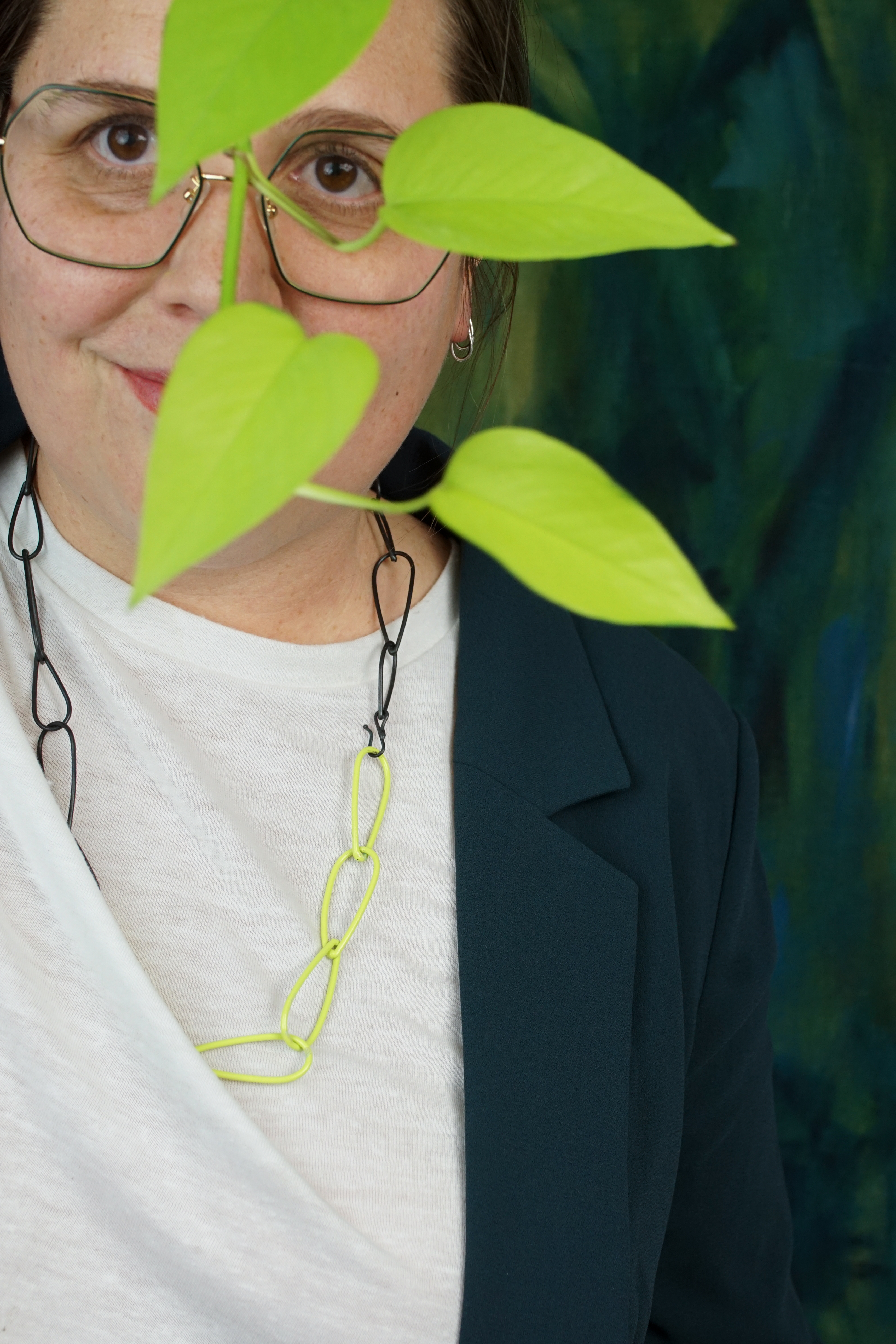 megan wearing green glasses with neon and steel chain necklace and neon pothos plant