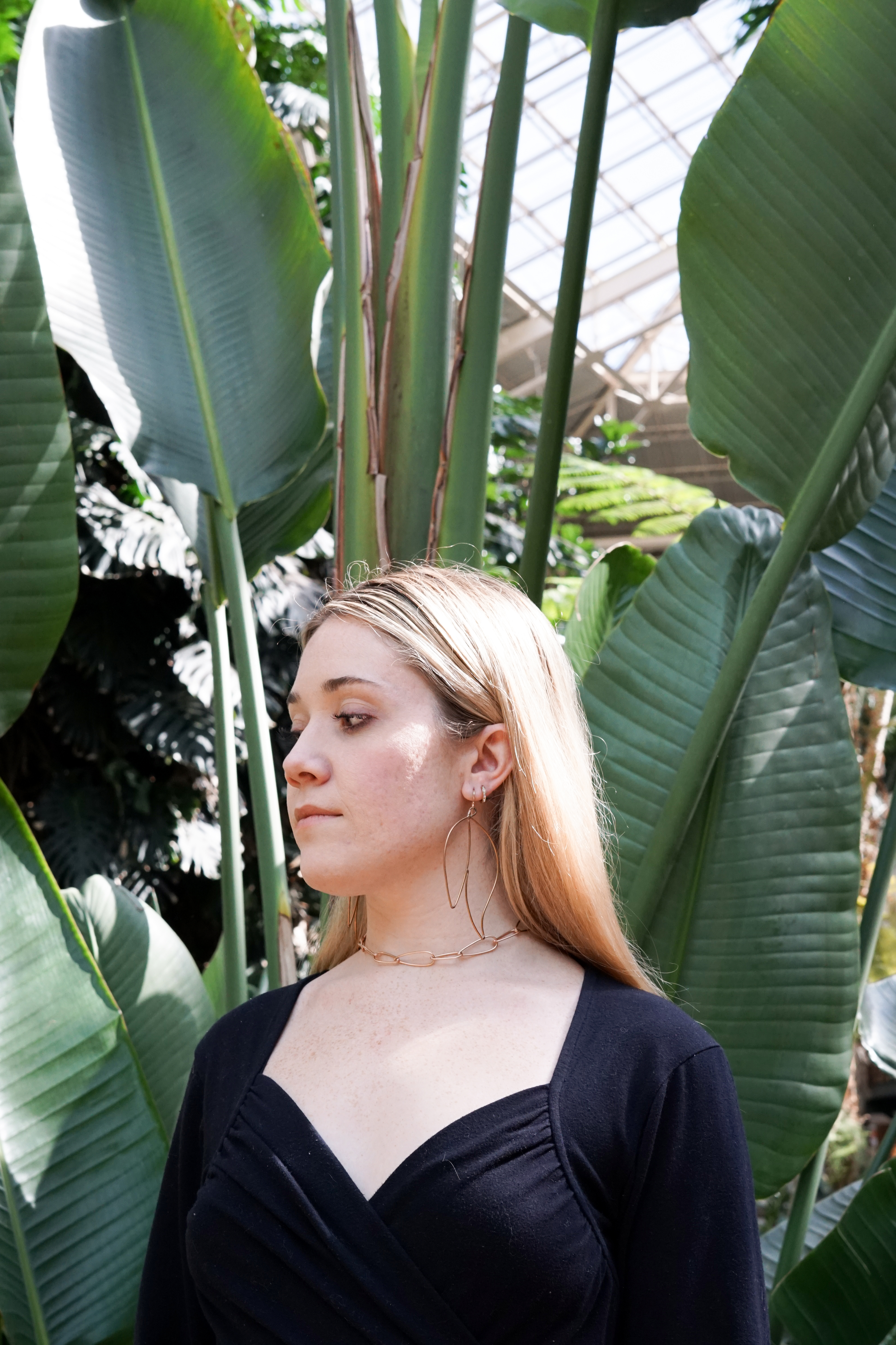 Trista surrounded by tropical plants wearing bronze statement earrings and bronze chain link necklace