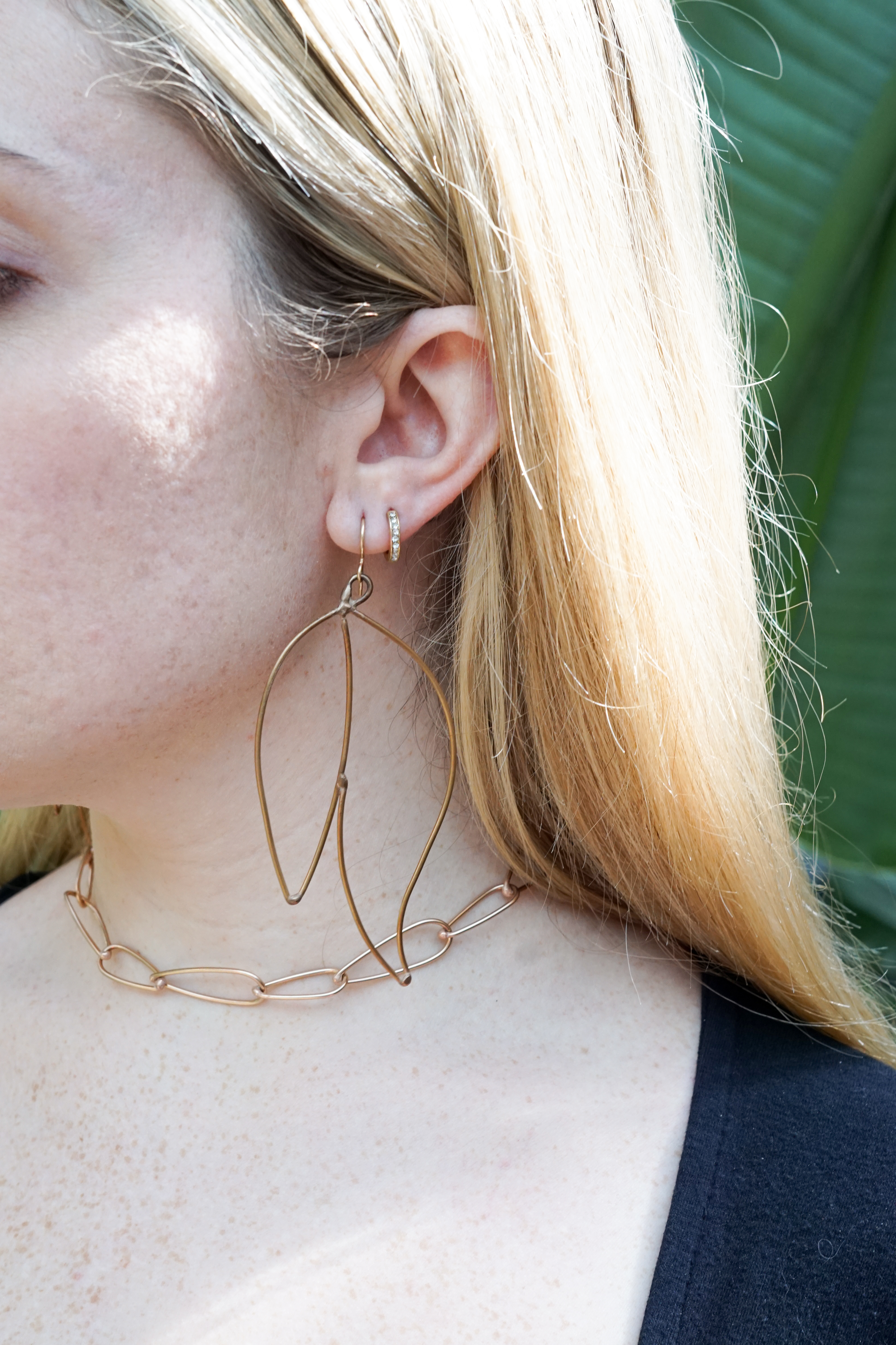 Trista surrounded by tropical plants wearing bronze statement earrings and bronze chain link necklace