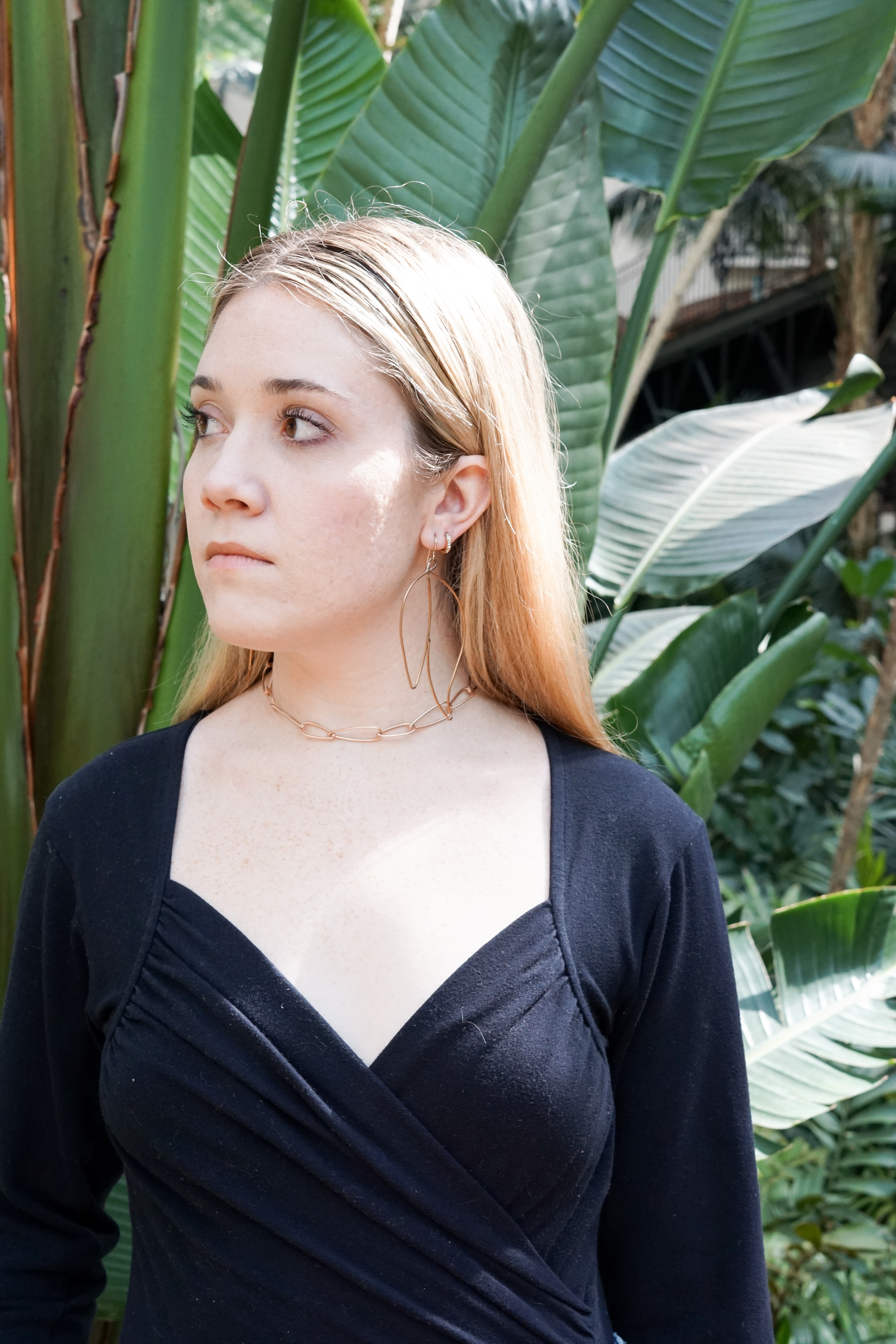 Trista surrounded by tropical plants wearing bronze statement earrings and bronze chain link necklace