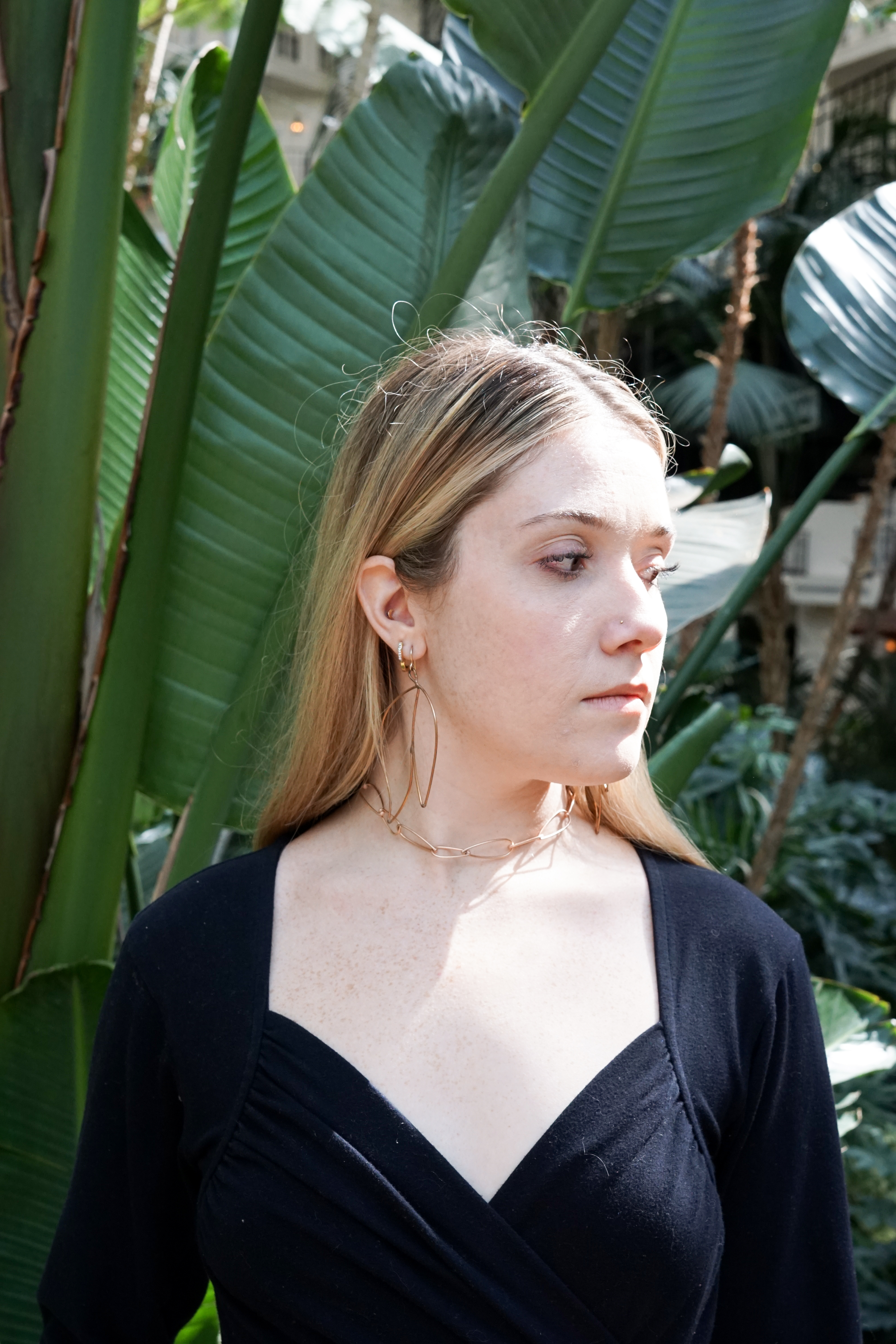 Trista surrounded by tropical plants wearing bronze statement earrings and bronze chain link necklace