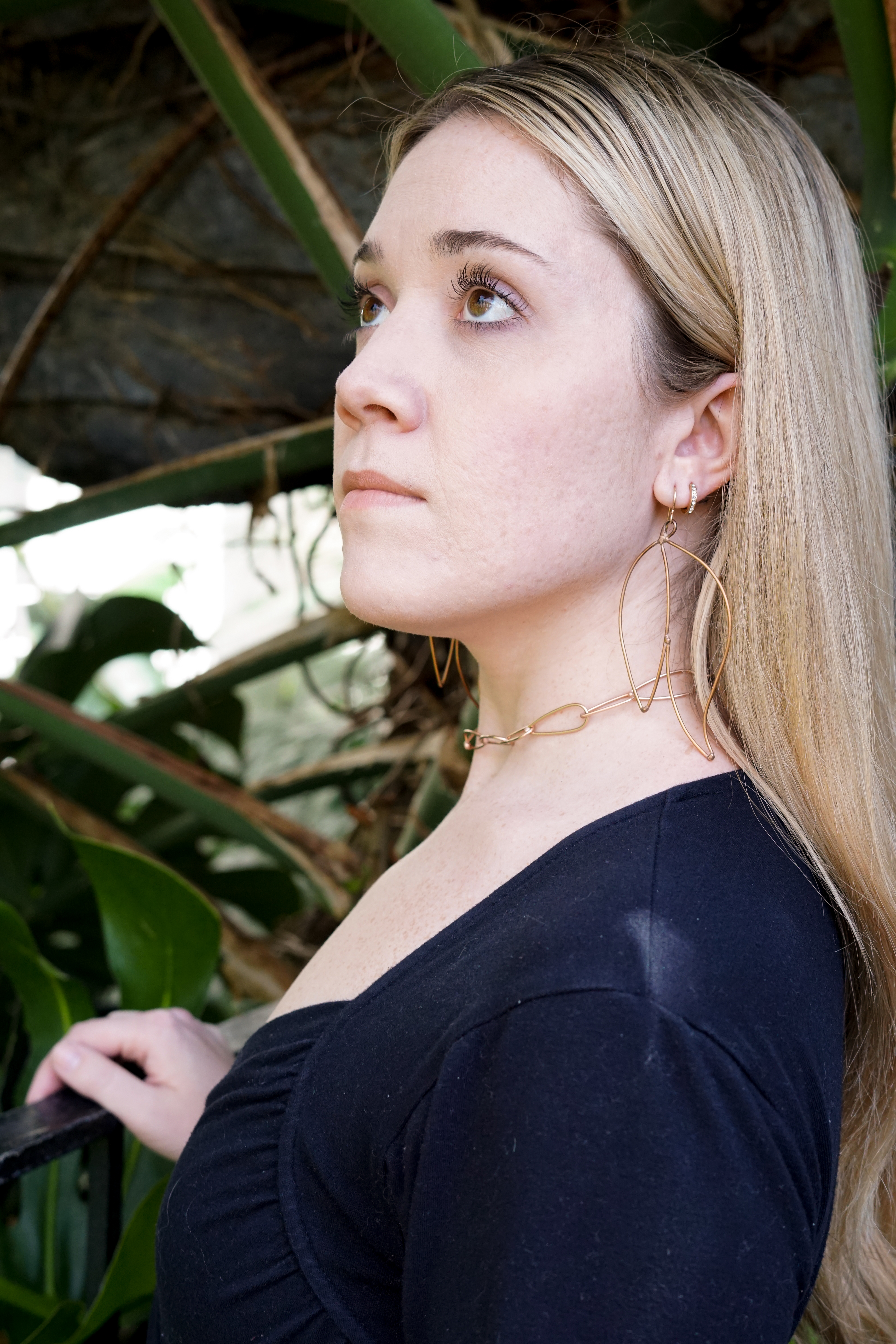 Trista in the garden wearing bronze statement earrings and bronze chain link necklace