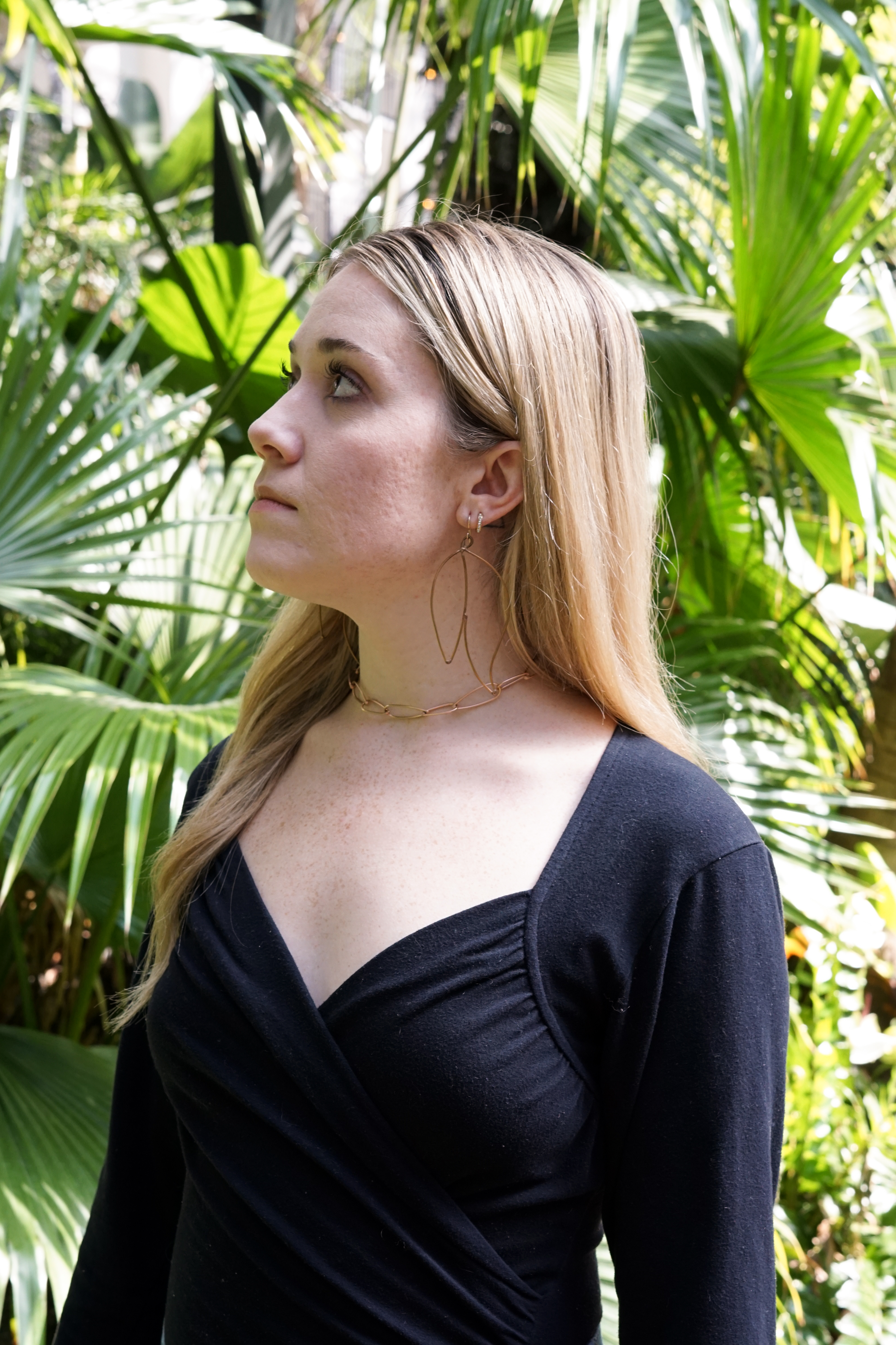 Trista surrounded by tropical plants wearing bronze statement earrings and bronze chain link necklace