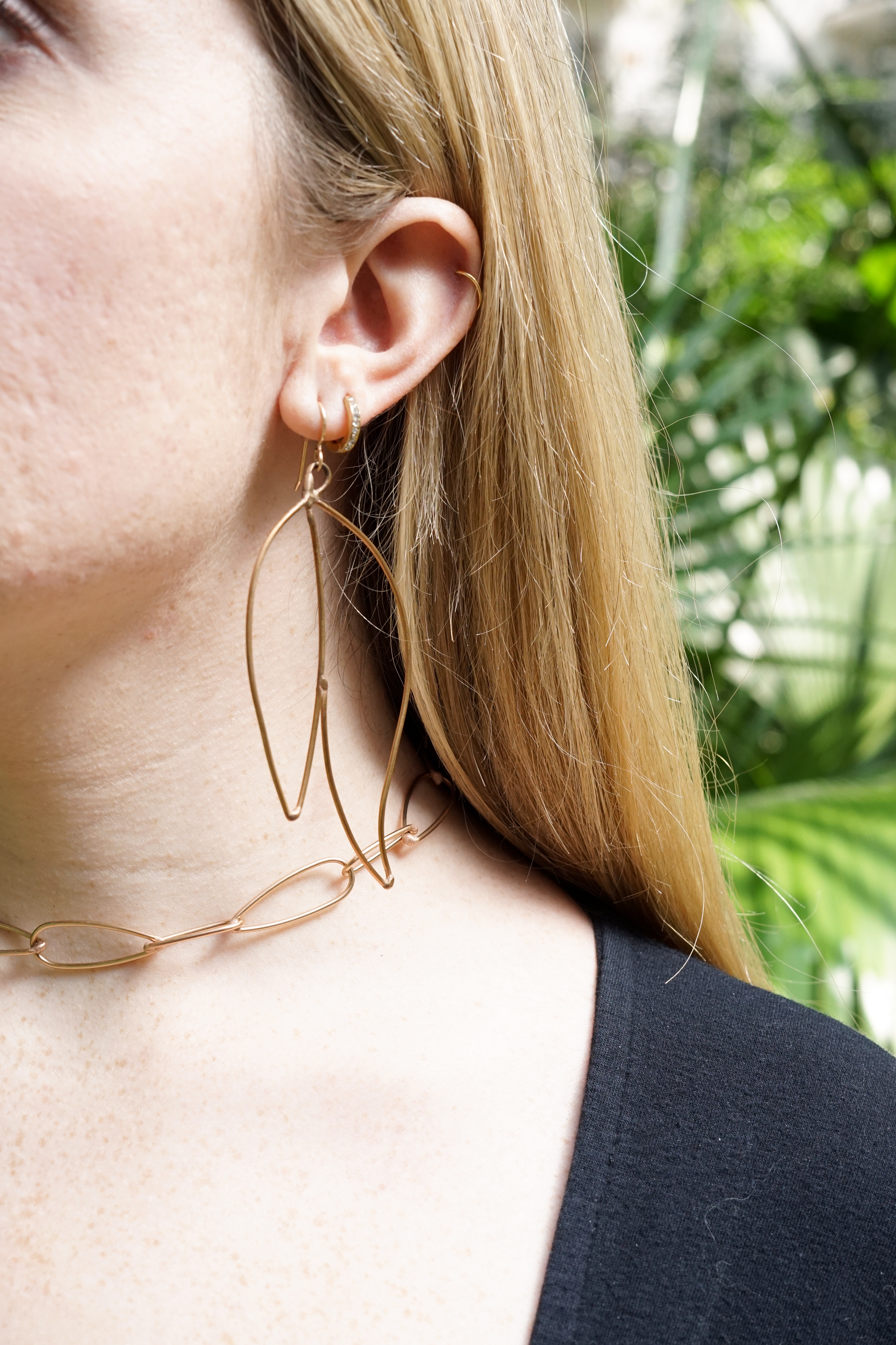 Trista surrounded by tropical plants wearing bronze statement earrings and bronze chain link necklace