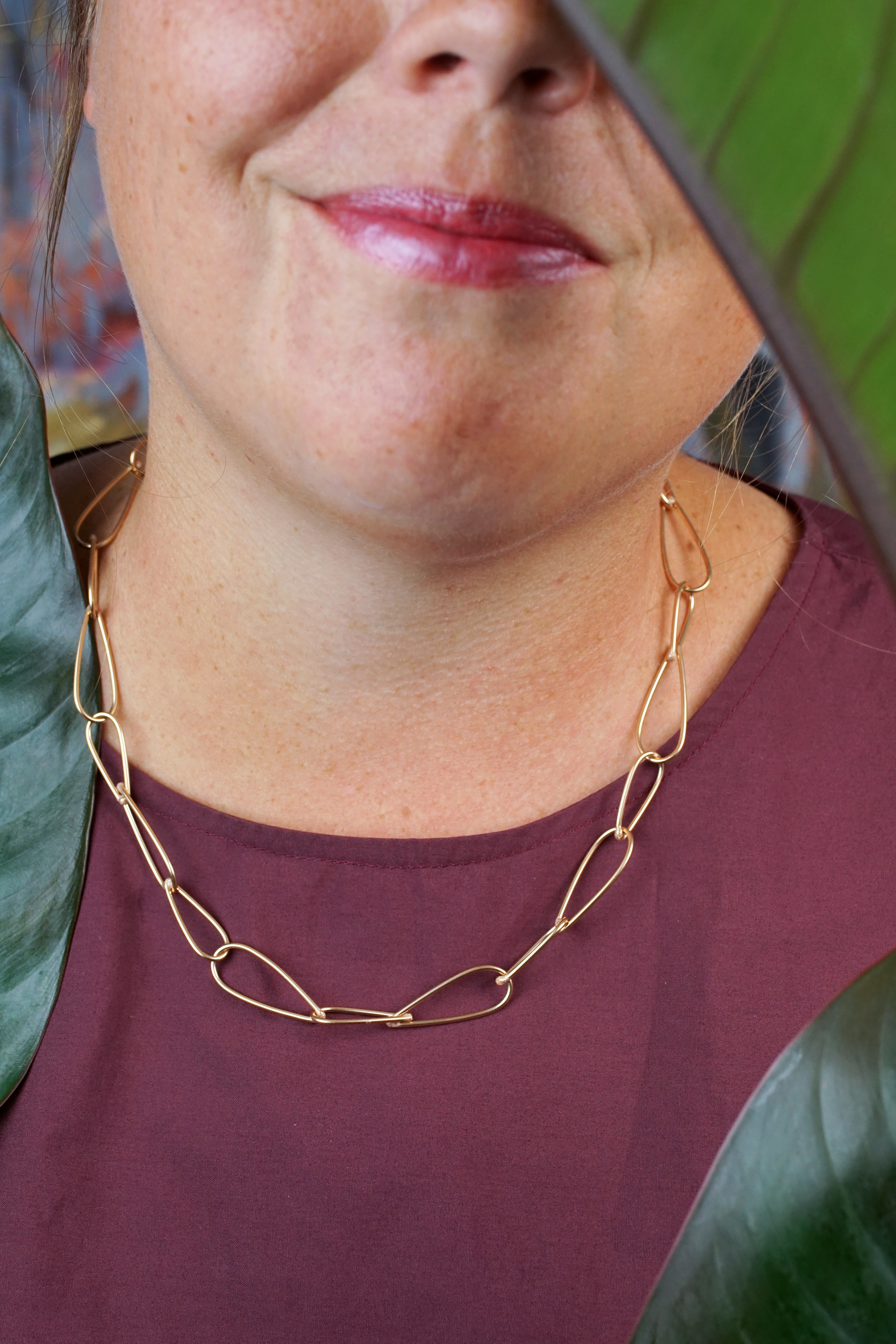 handcrafted bronze chain necklace, burgundy dress, and philodendron rojo congo