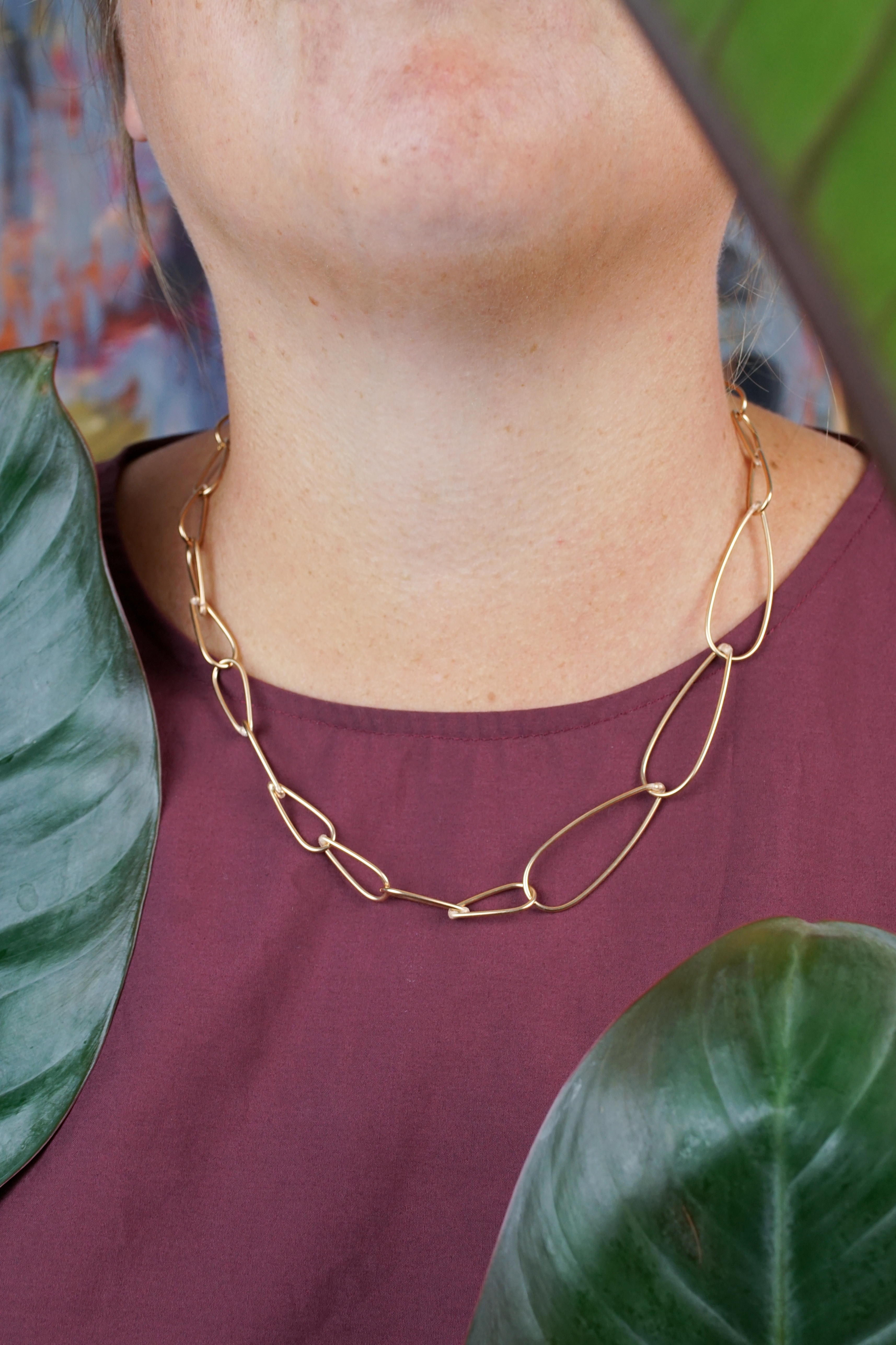 handcrafted bronze chain necklace, burgundy dress, and philodendron rojo congo