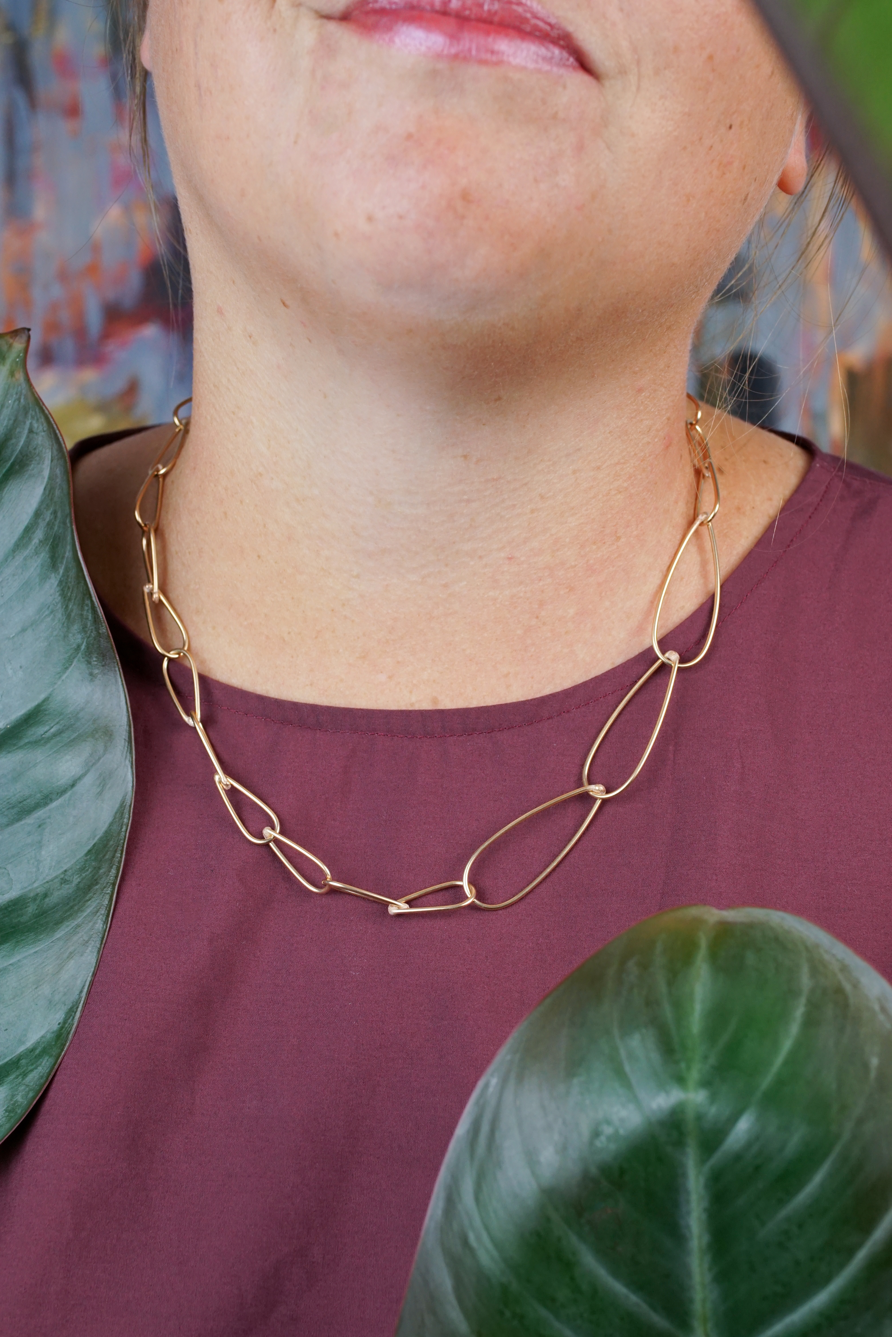 handcrafted bronze chain necklace, burgundy dress, and philodendron rojo congo